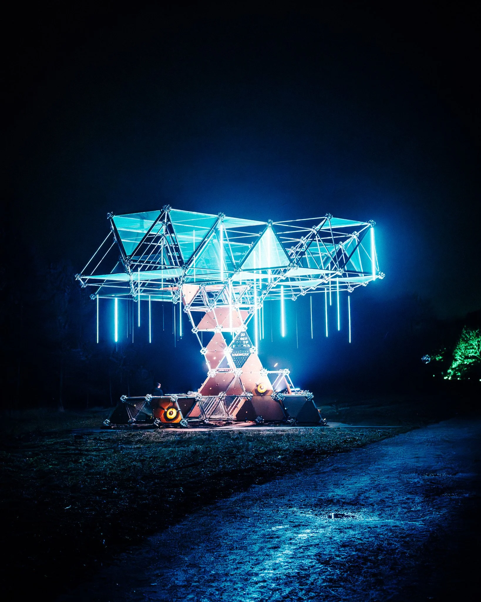 Verlichte attractie in een pretpark 's nachts, structuurelementen en water reflecteren het licht.