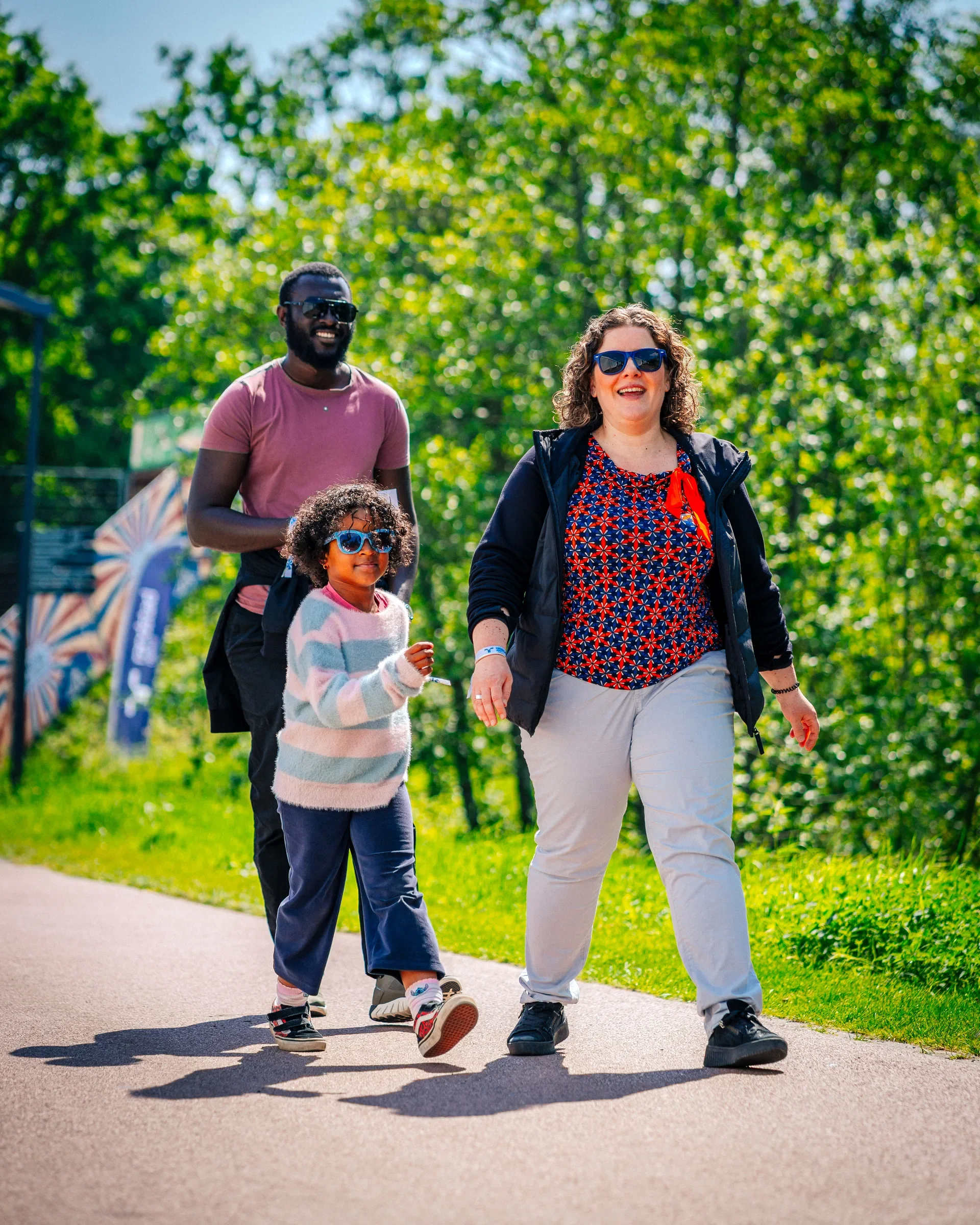 Gezellig gezin wandelen in park op zonnige dag, meisje op skateboard, grote vrouw en man met zonnebrillen.