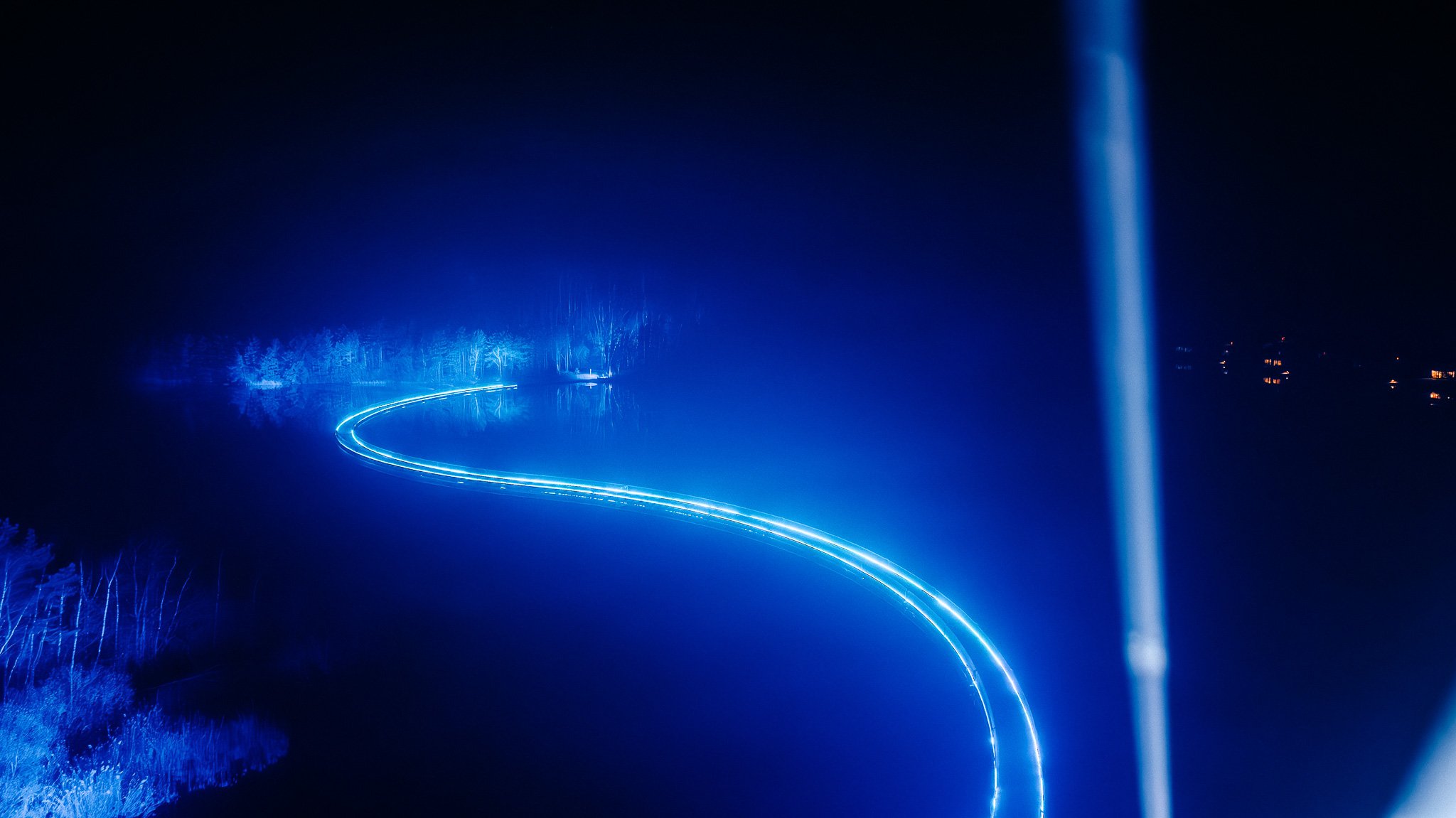Lichtsporen en waterfallets bij nacht, met blauwe en witte lichtlijnen over een donker landschap.