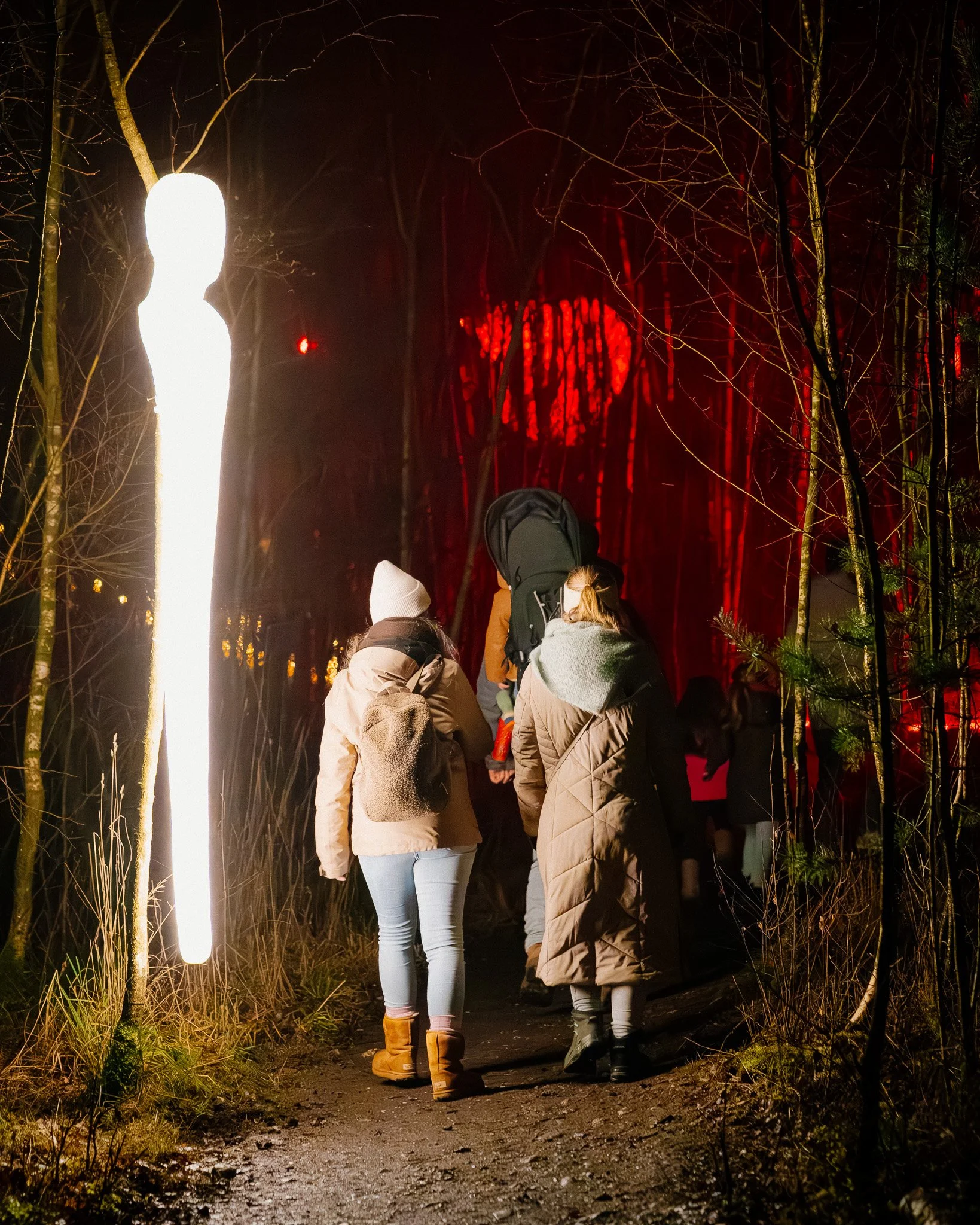 Groep mensen wandelt 's avonds door een bos met verlichte paden, gekleed in jassen en winterschoenen.