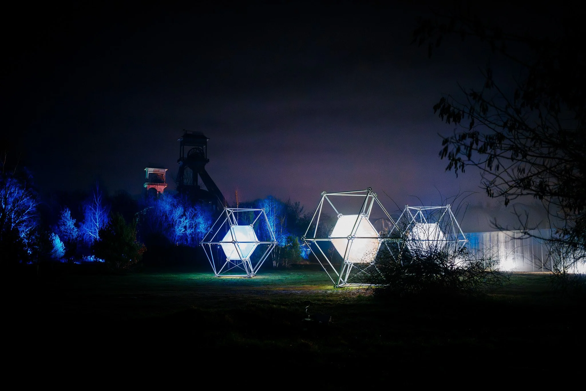 Verlichte kunstinstallaties en constructies in een nachtelijk park onder een donkere hemel.