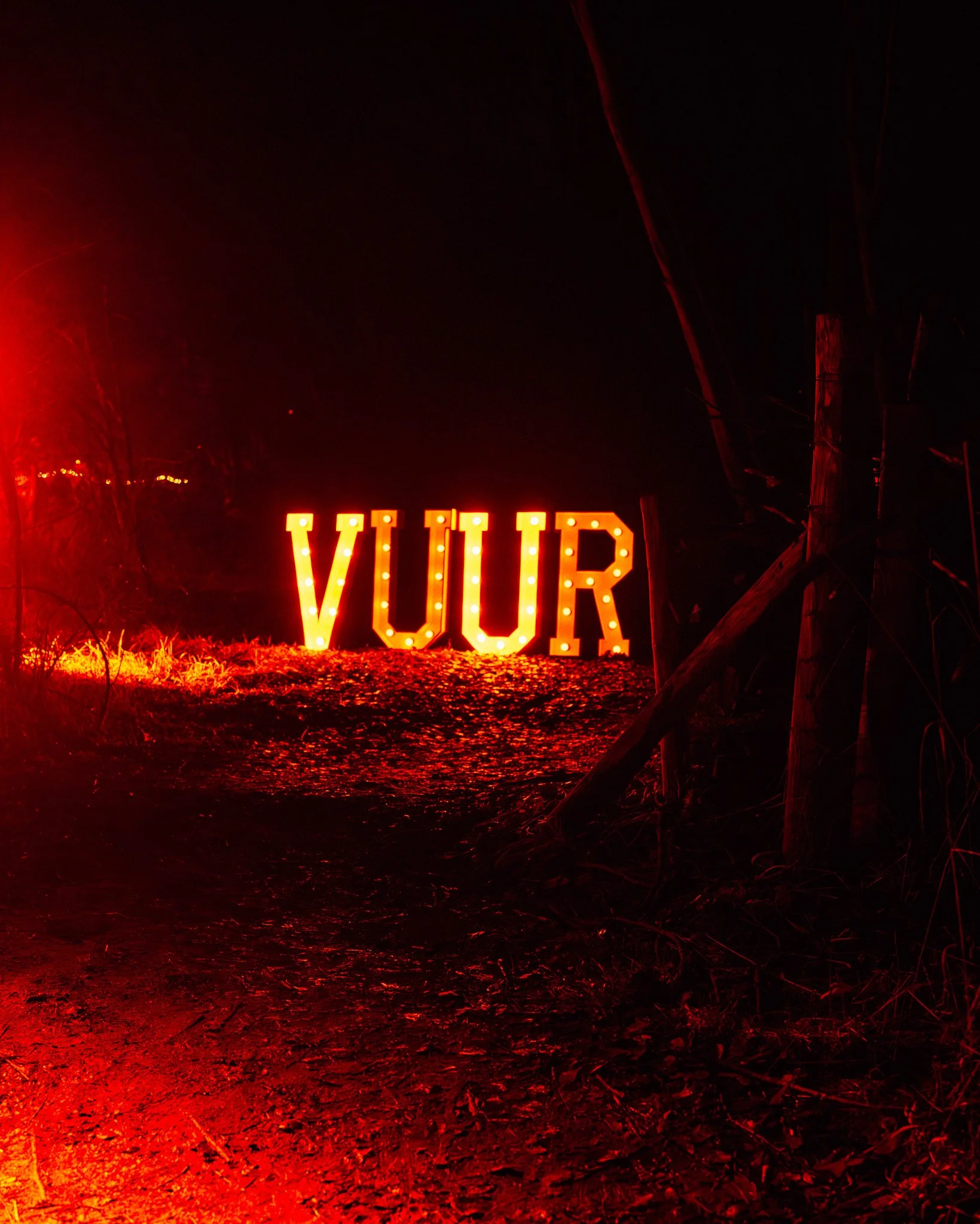 Verlichte letters die het woord 'VUIR' vormen, geplaatst op de grond bij nacht met een rood/oranje gloed