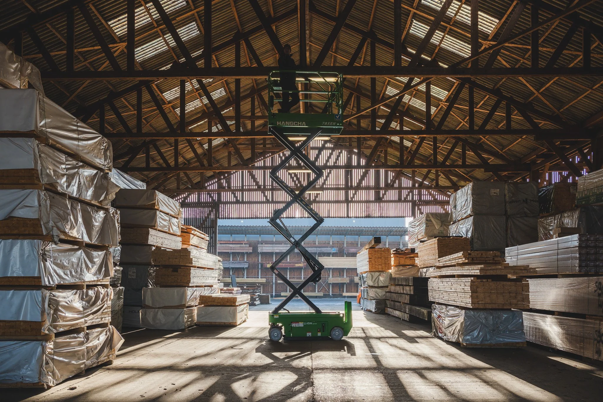 Hoogwerker tussen hoge stapels hout in een industriële loods