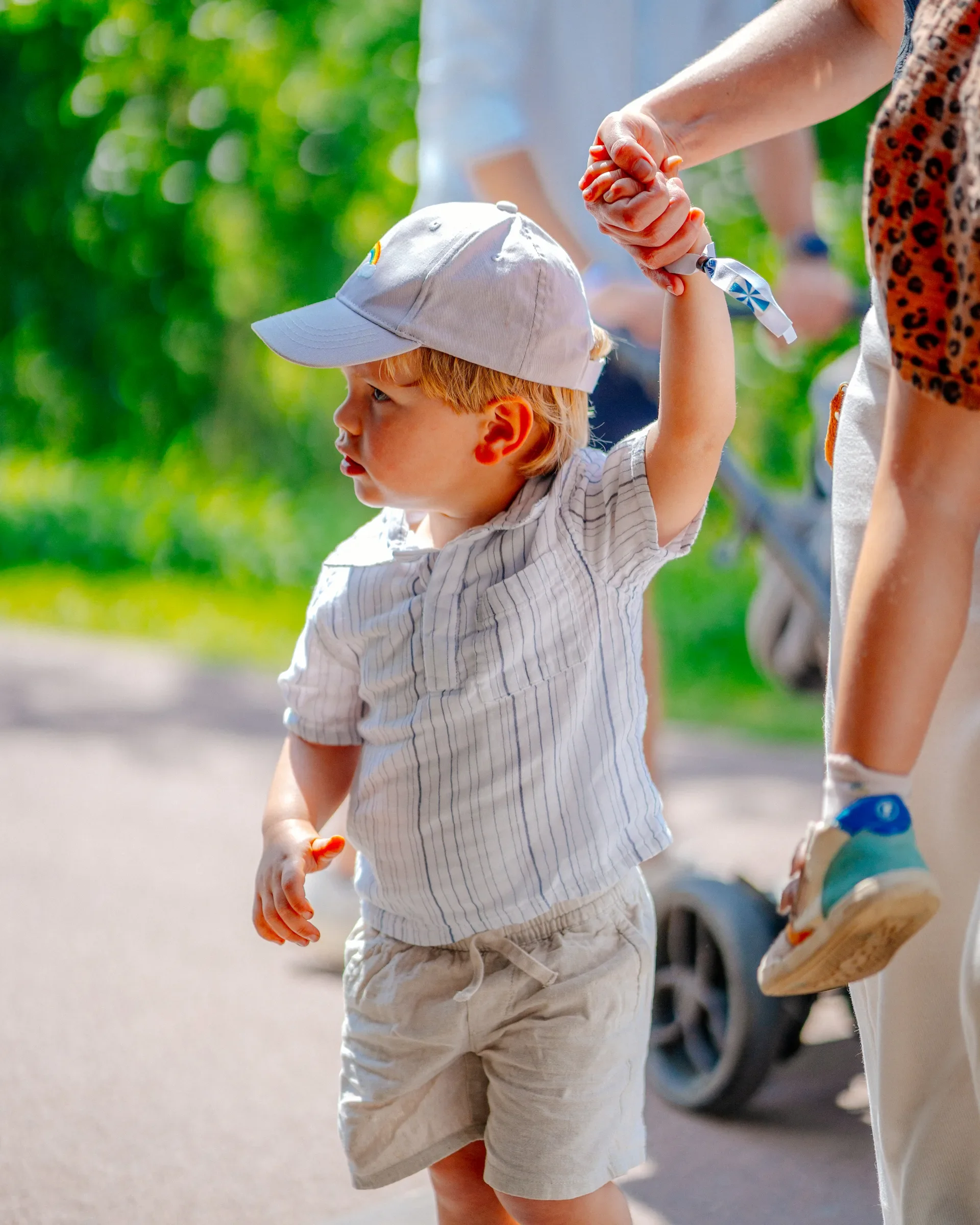 Close-up van een jonge jongen die hand in hand loopt met een volwassene, beide hand in hand, in een groene buitenomgeving.