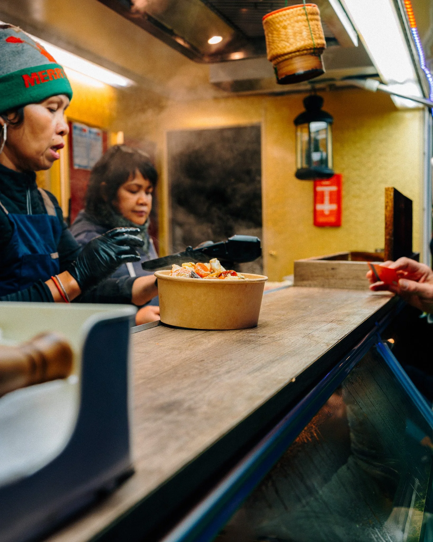 Twee mensen bestellen pizza bij een restaurant. Er staat een grote bak met pizza op de toonbank.