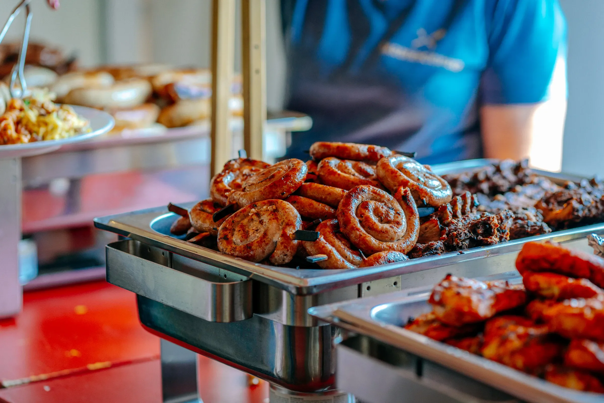 Gebakken worstjes en barbecuevlees op een buffet met andere warme gerechten op de achtergrond.