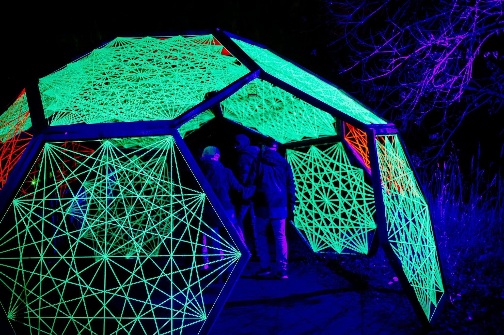 Mensen die naar een verlichte kunstinstallatie kijken in de nacht.