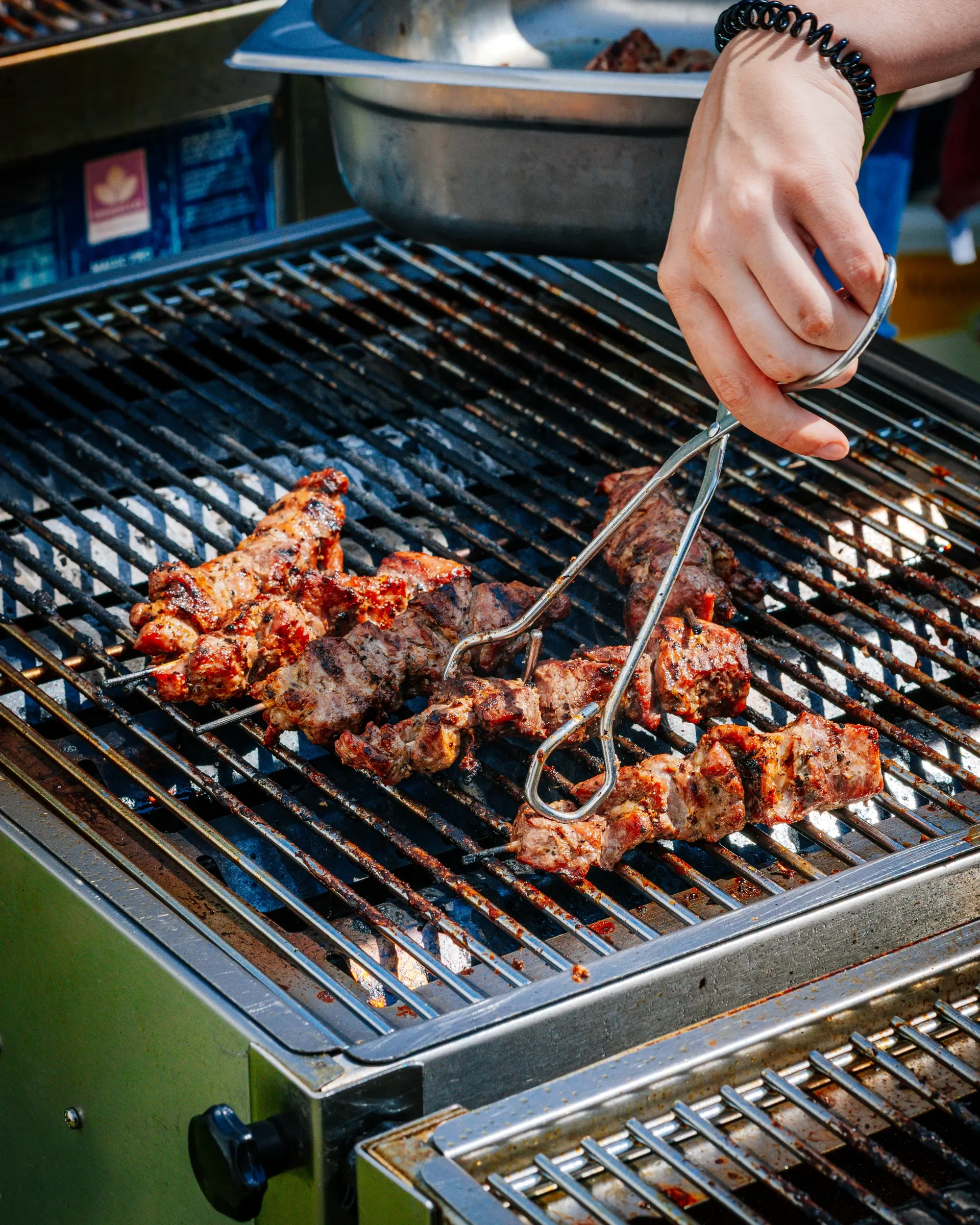 Een barbecue met vlees dat wordt gegrild, een persoon gebruikt een tang om het vlees te draaien.