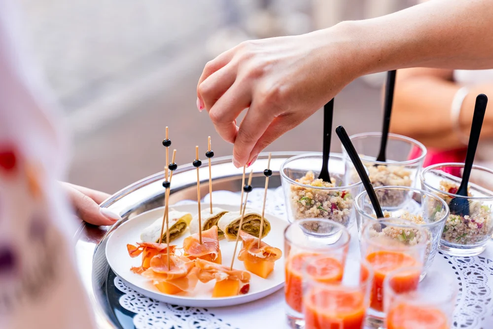 Close-up van hapjes en oranje drankjes op een plateau tijdens Bella Dita opening