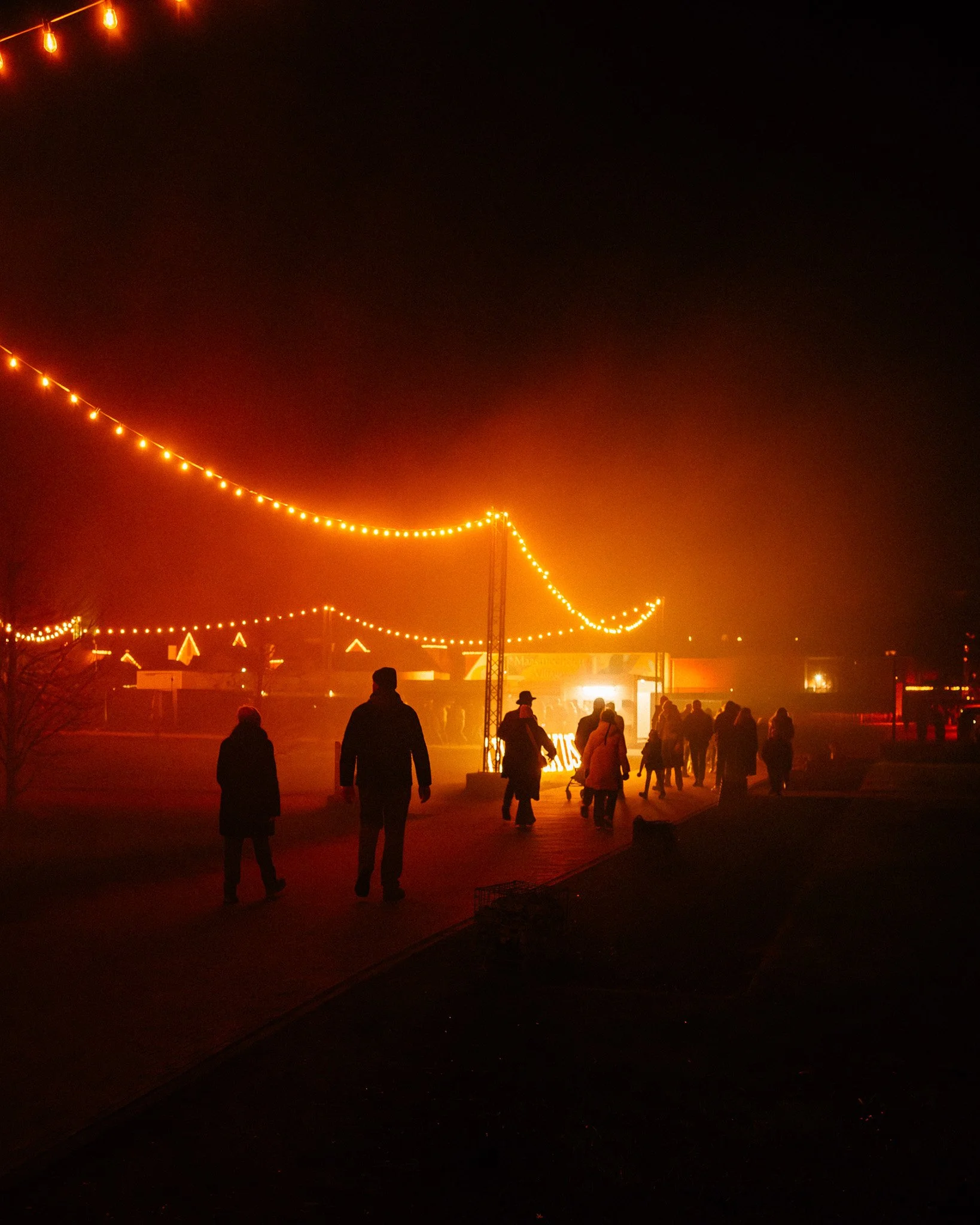 Mensen wandelen onder oranje verlichte feestverlichting tijdens de avond.