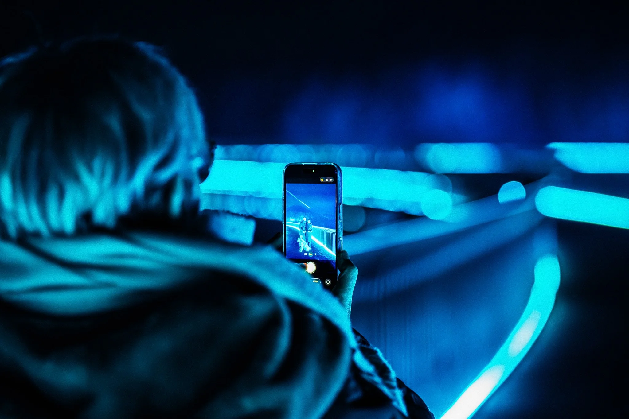 Een persoon neemt een foto of video van een standbeeld of een figuur met een smartphone in een kamer met blauwe verlichting.
