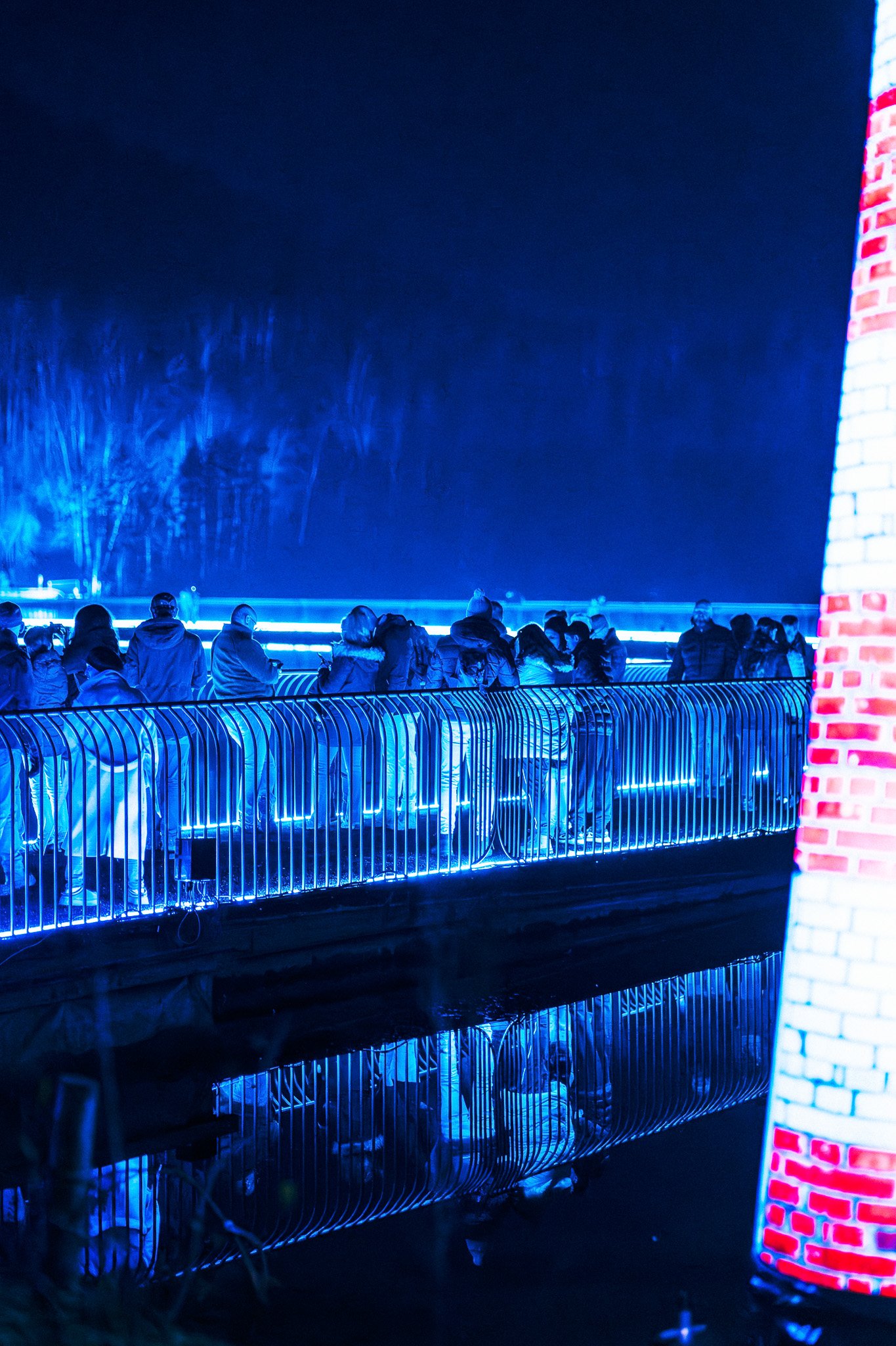 Gezichtspunt op een groep mensen die naar een verlichte brug staan te kijken tijdens de nacht.