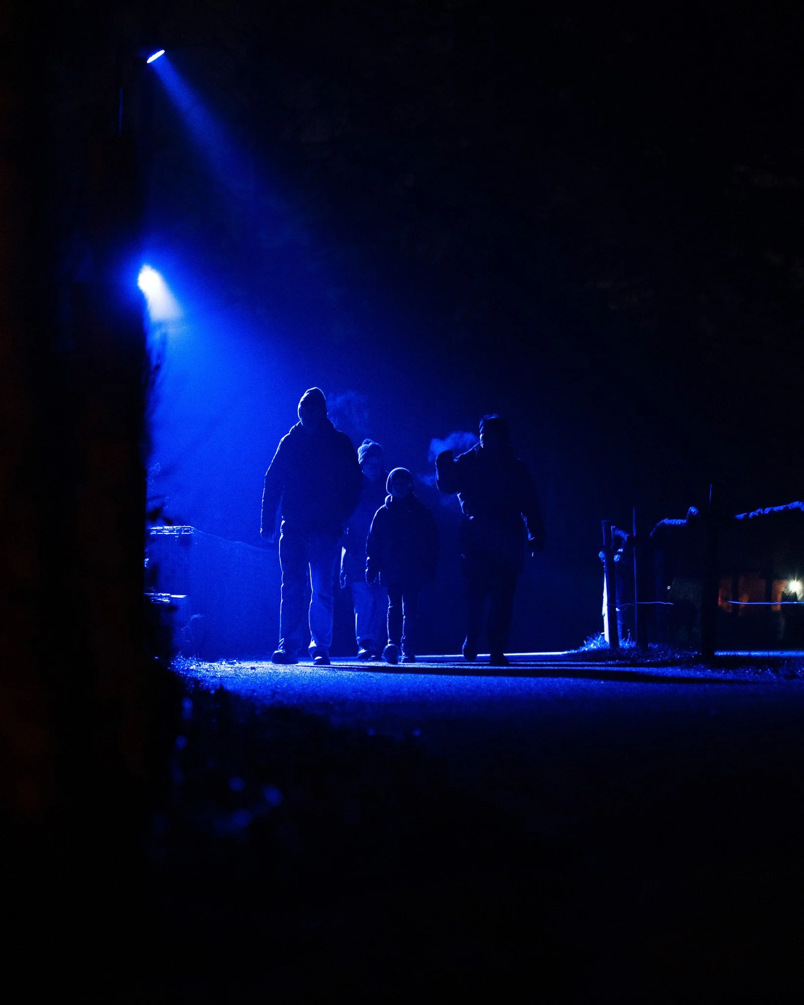 Mensen lopen onder blauwe lichtprojecties op een donkere achtergrond.