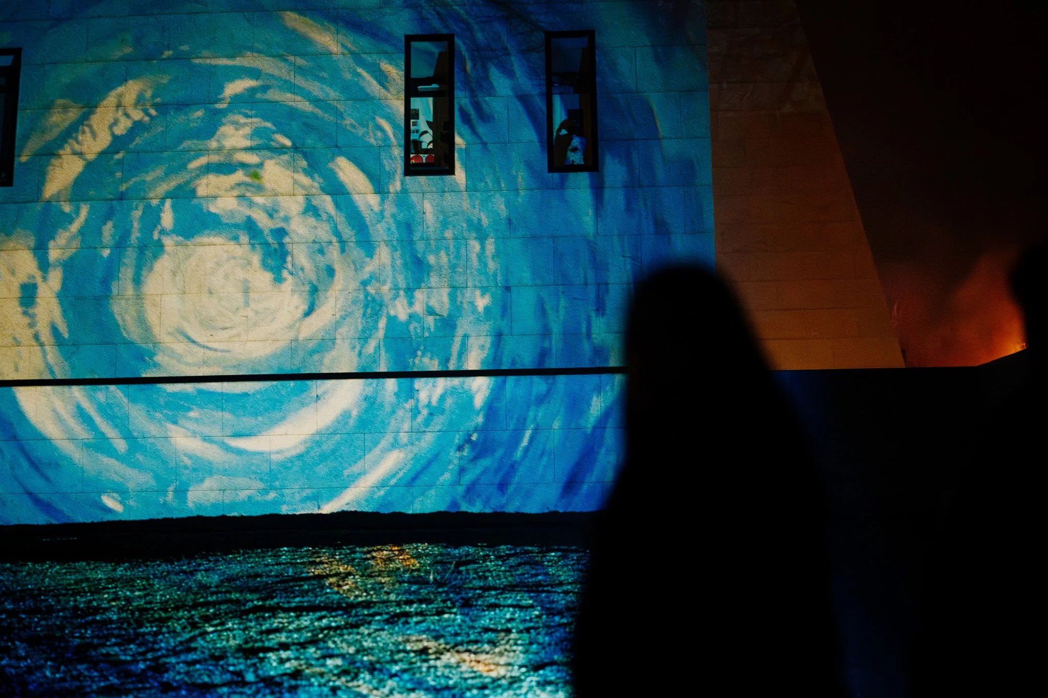 Een muur met een grote projectie van een schilderachtige zee en een stormachtige wolkenlucht, met een reflectie in het water eronder.