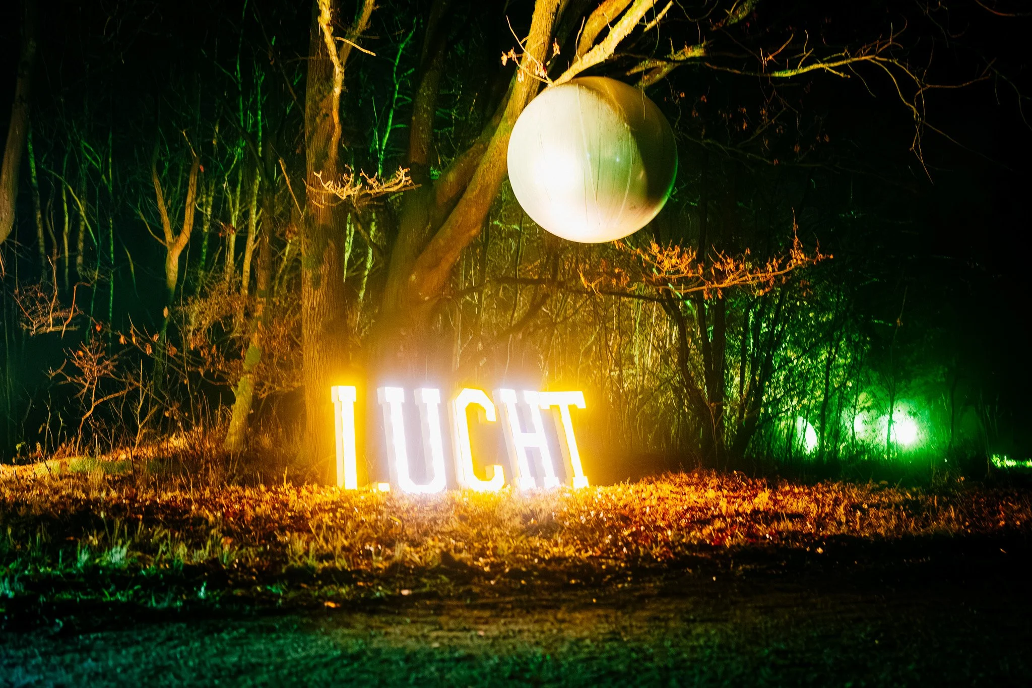 Verlichte bomen met een grote lichtgevende bal en een neonverlichting die 'LUCHT' spellen.