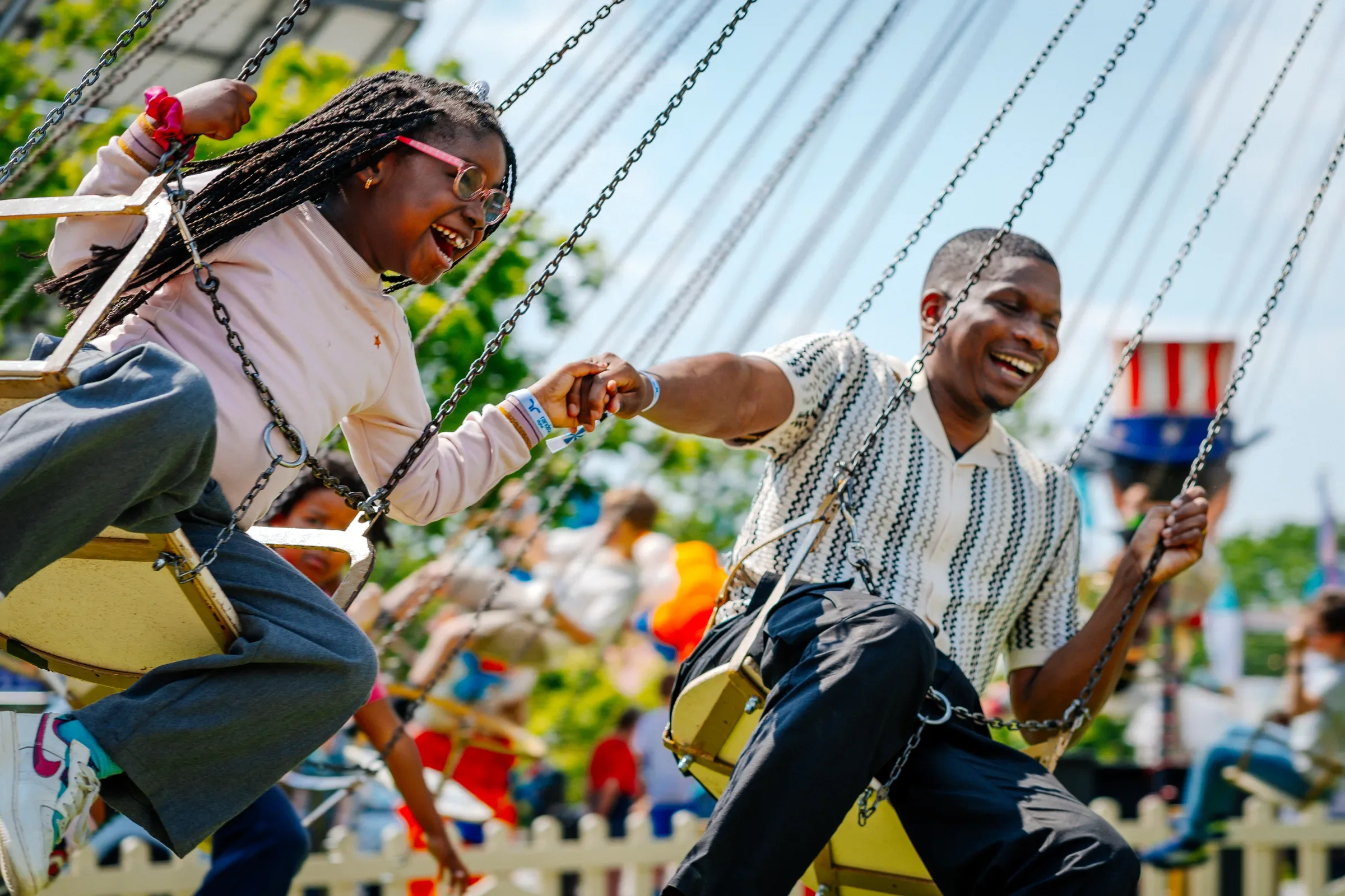 Twee mensen genieten van een schommel op een kermis of pretpark, ze houden elkaars handen vast en lachen.