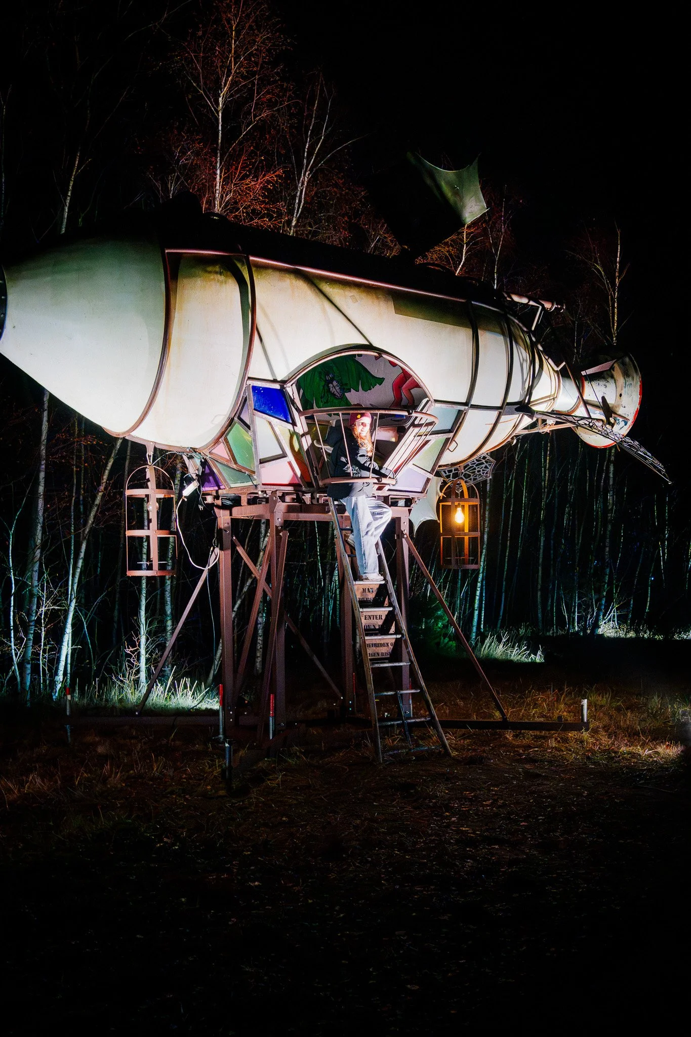 Een verlichte heliumballon boven een donker bos in de nacht, met een persoon die in de ballon zit en omringd is door bomen.