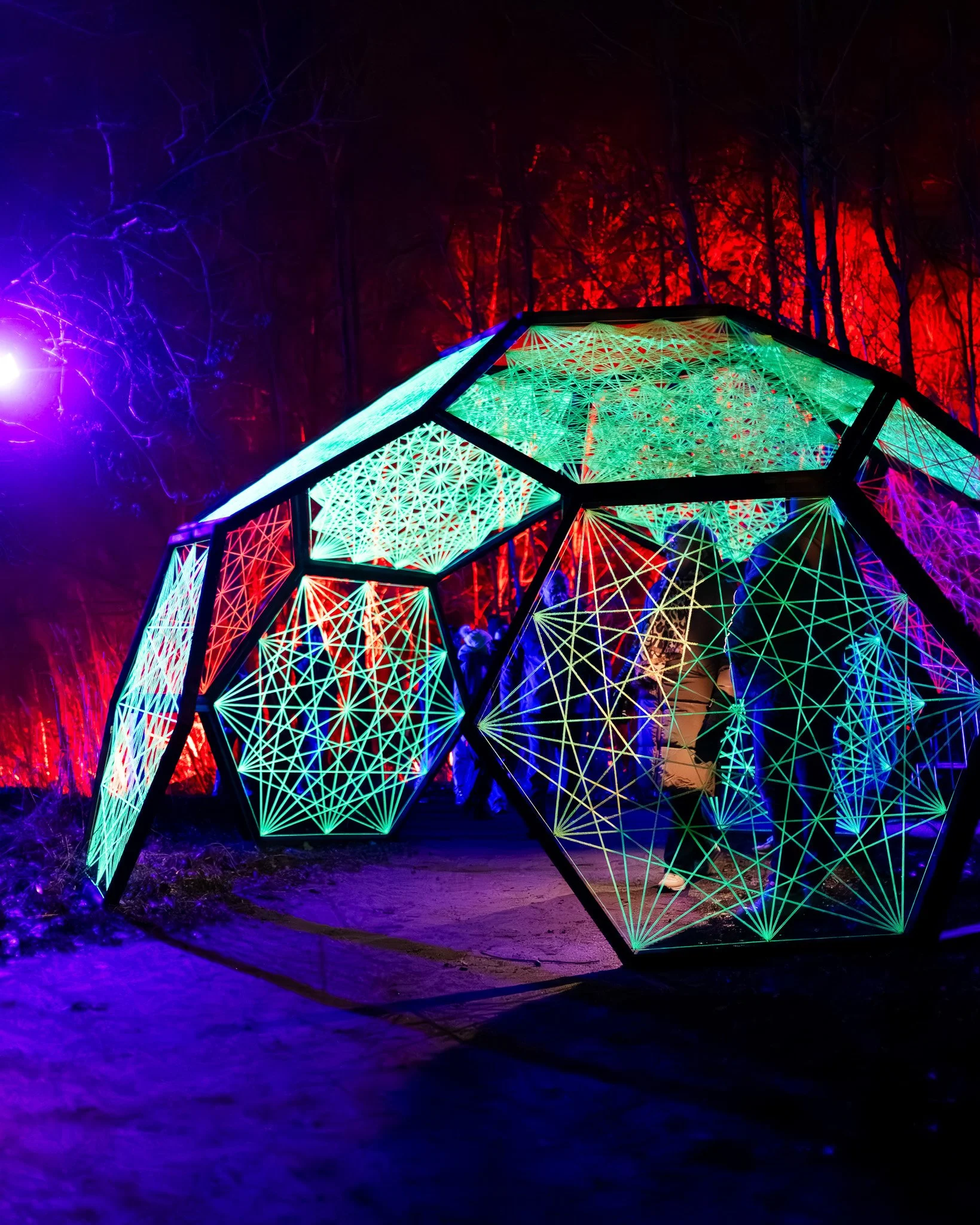 Een lichtinstallatie met geometrische vormen en kleurrijke LEDs in een donkere omgeving, met rode en blauwe achtergrondverlichting en een koele glow op de grond.