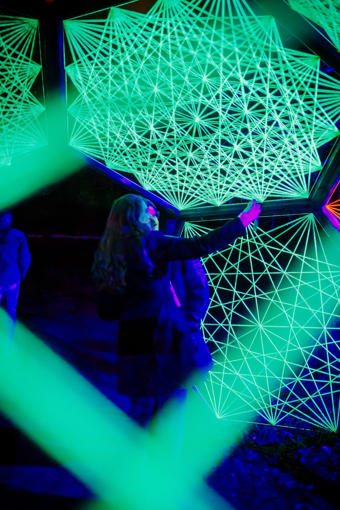 Mensen die kijken naar een neon lichtkunstwerk met geometrische patronen in groen en blauw.