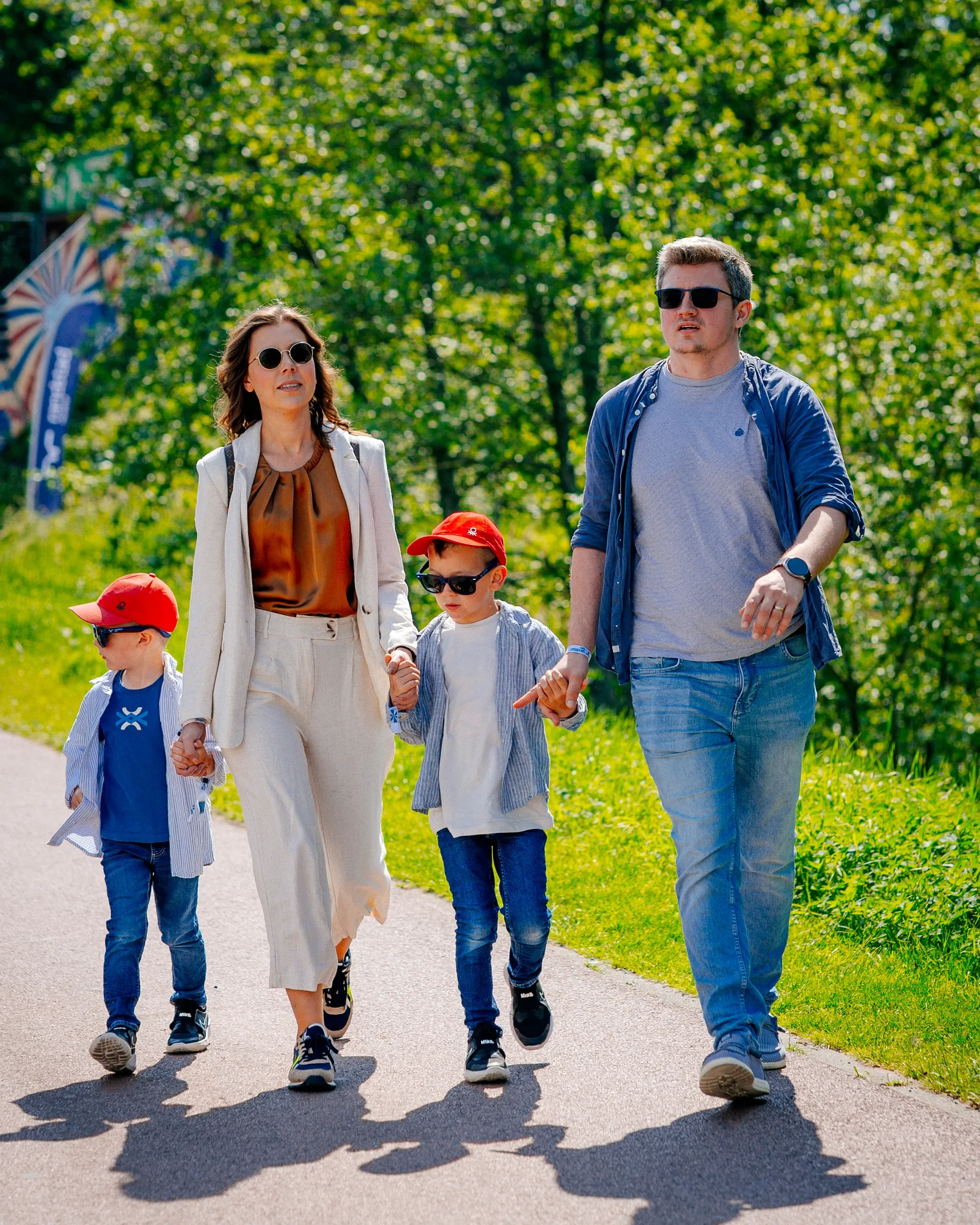 Gezin van vier personen, ouders en kinderen, wandelen in een park op een zonnige dag.