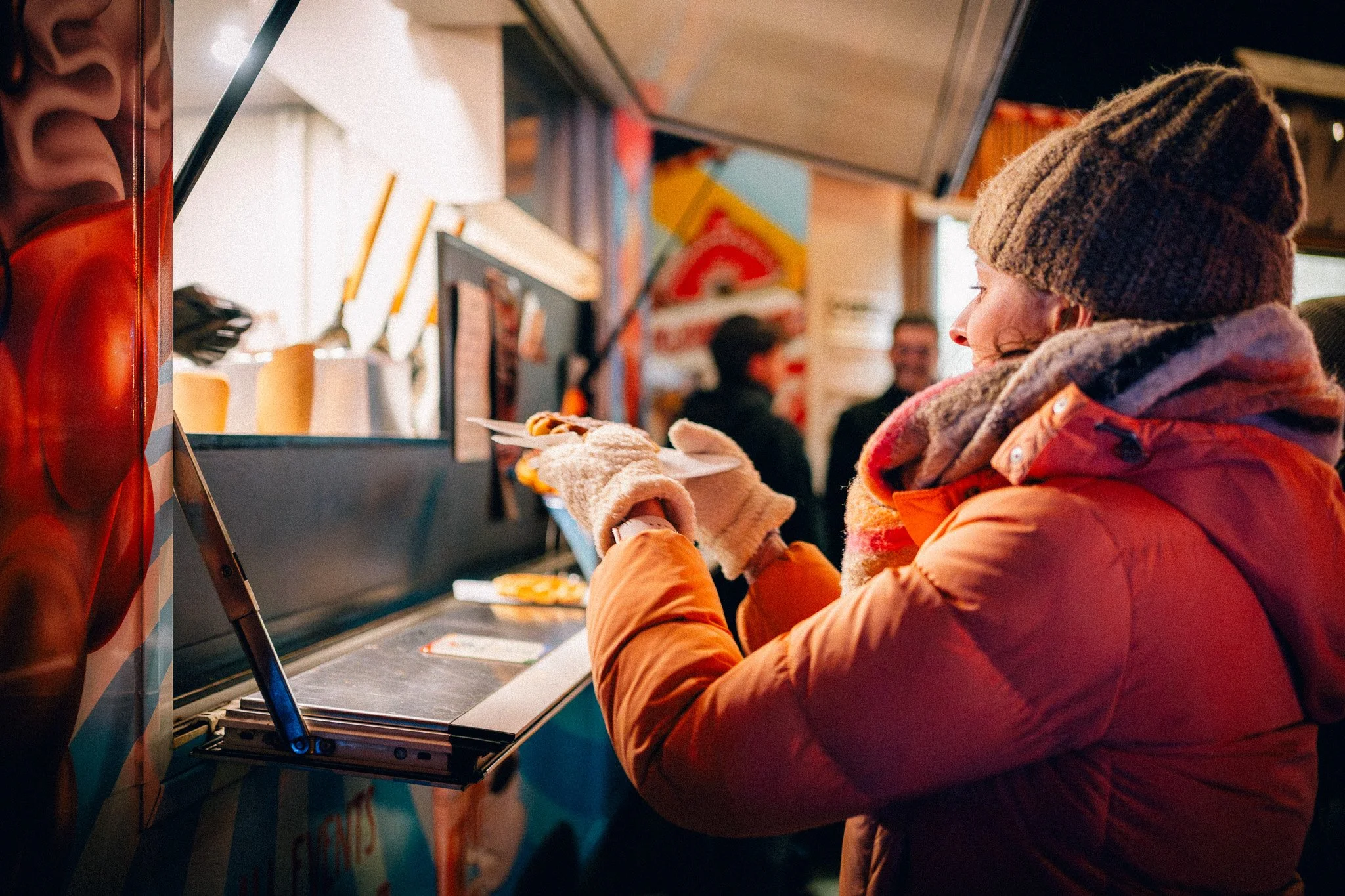 Een vrouw in een warm jasje en trui bestelt voedsel bij een foodtruck.