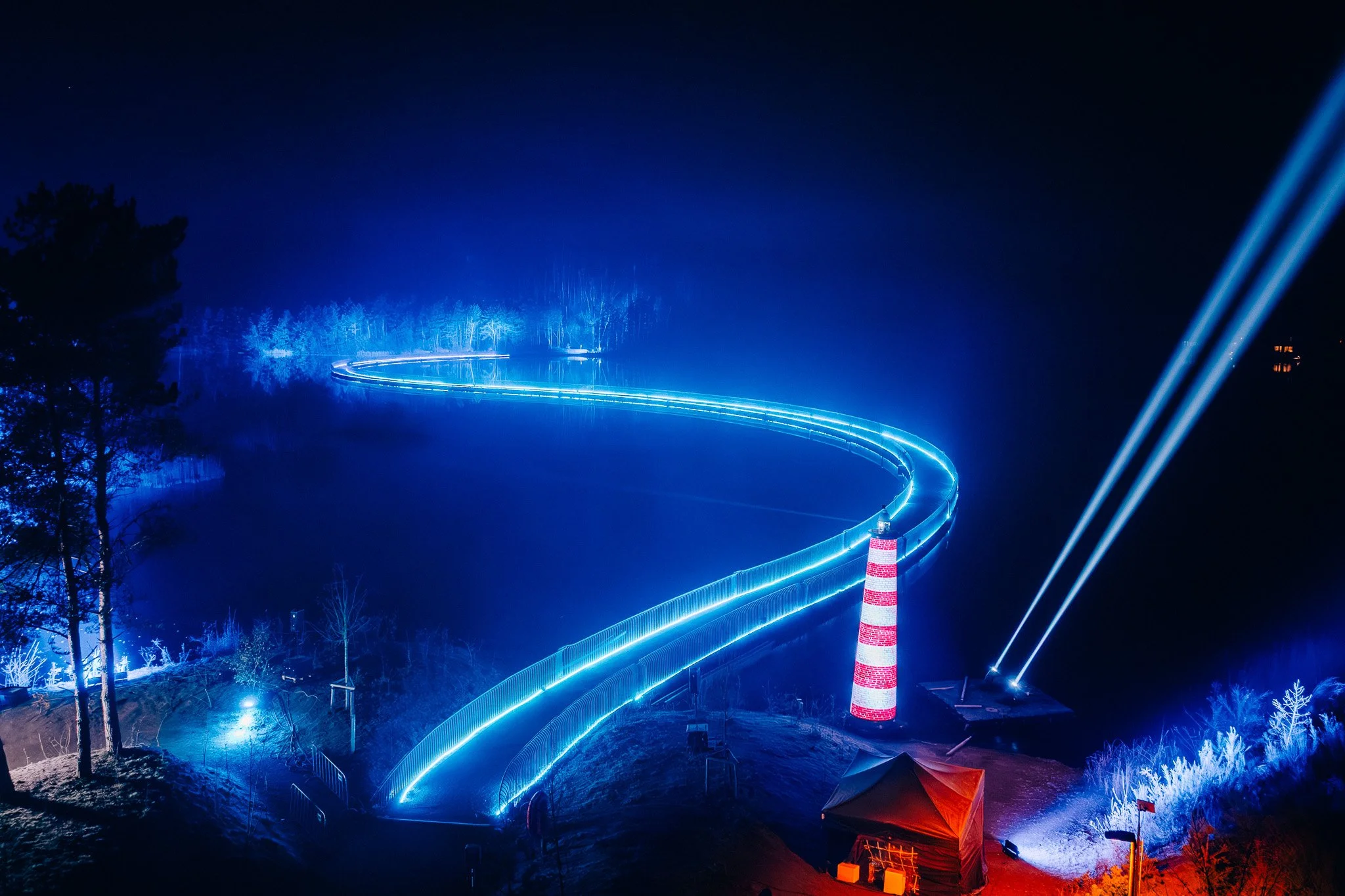 Lichtspoor in de nacht met blauwe verlichting, een verkeersvlag en enkele tenten op de grond.