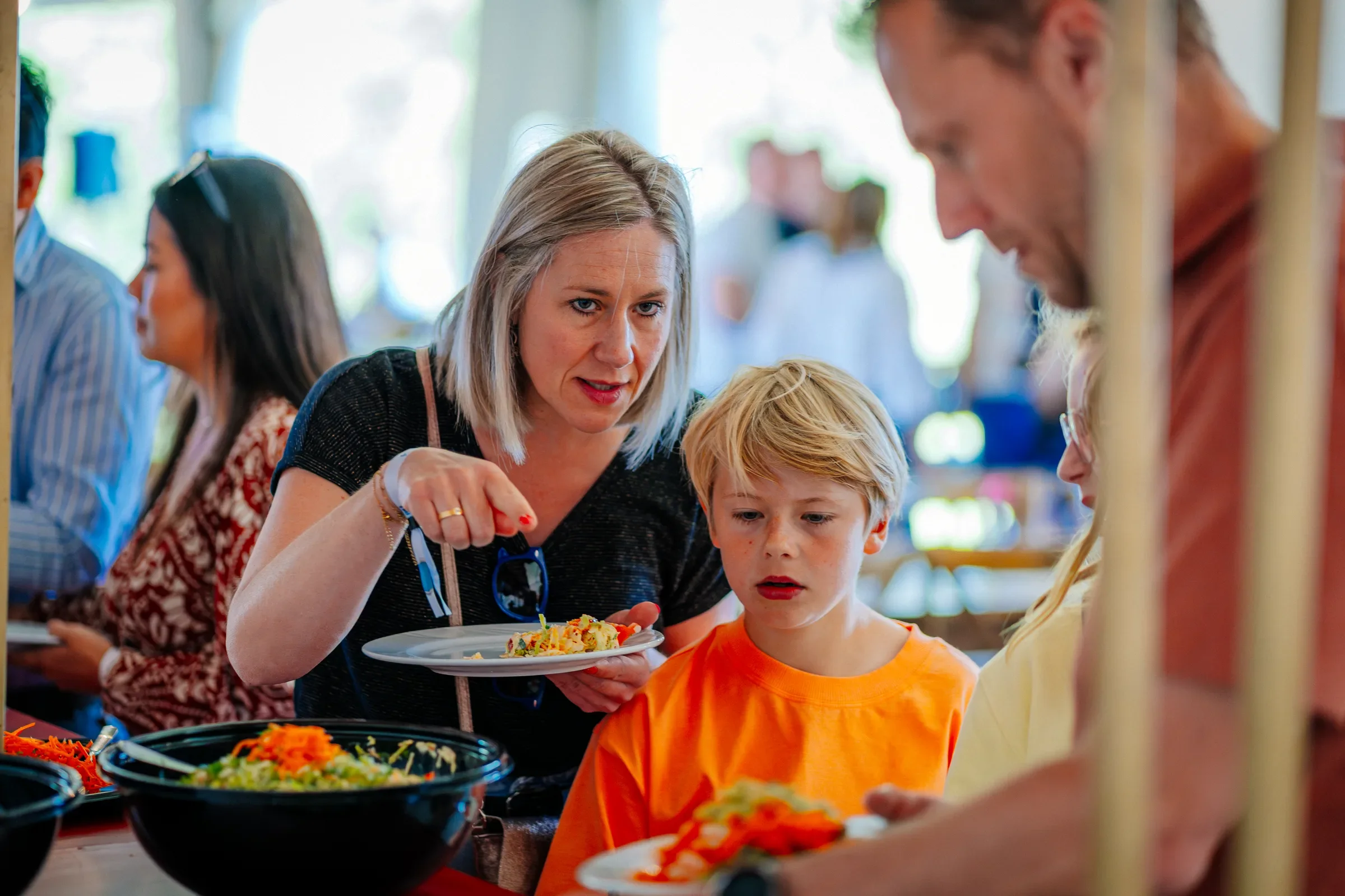 Mensen die bij een buffet serveren en eten uitkiezen, met een vrouw en een jongen in focus.