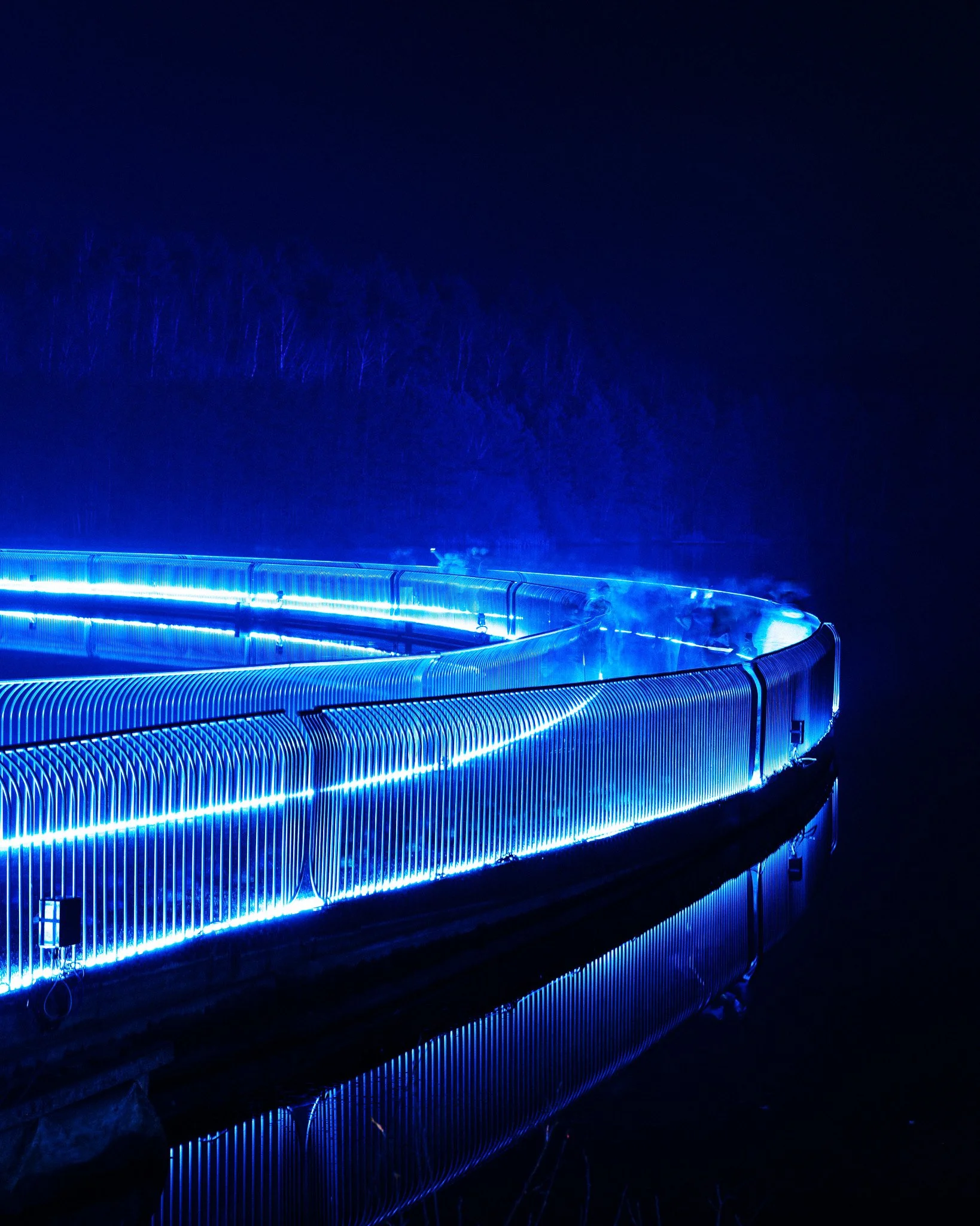 Een nachtzicht van een waterglijbaan met blauwe LED-verlichting, omgeven door donkere bomen en een nachtelijke hemel.