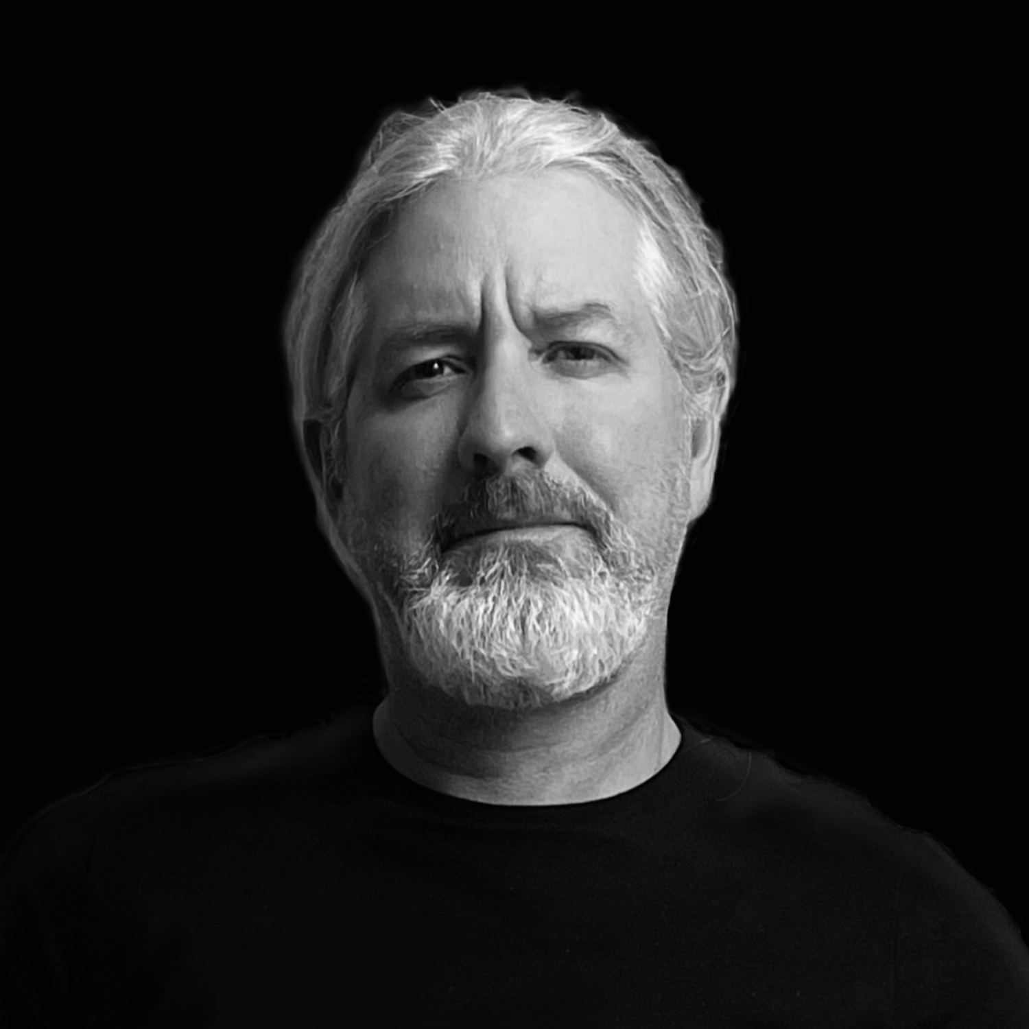 Black and white portrait of a man with a beard and mustache, wearing a dark shirt, set against a black background.