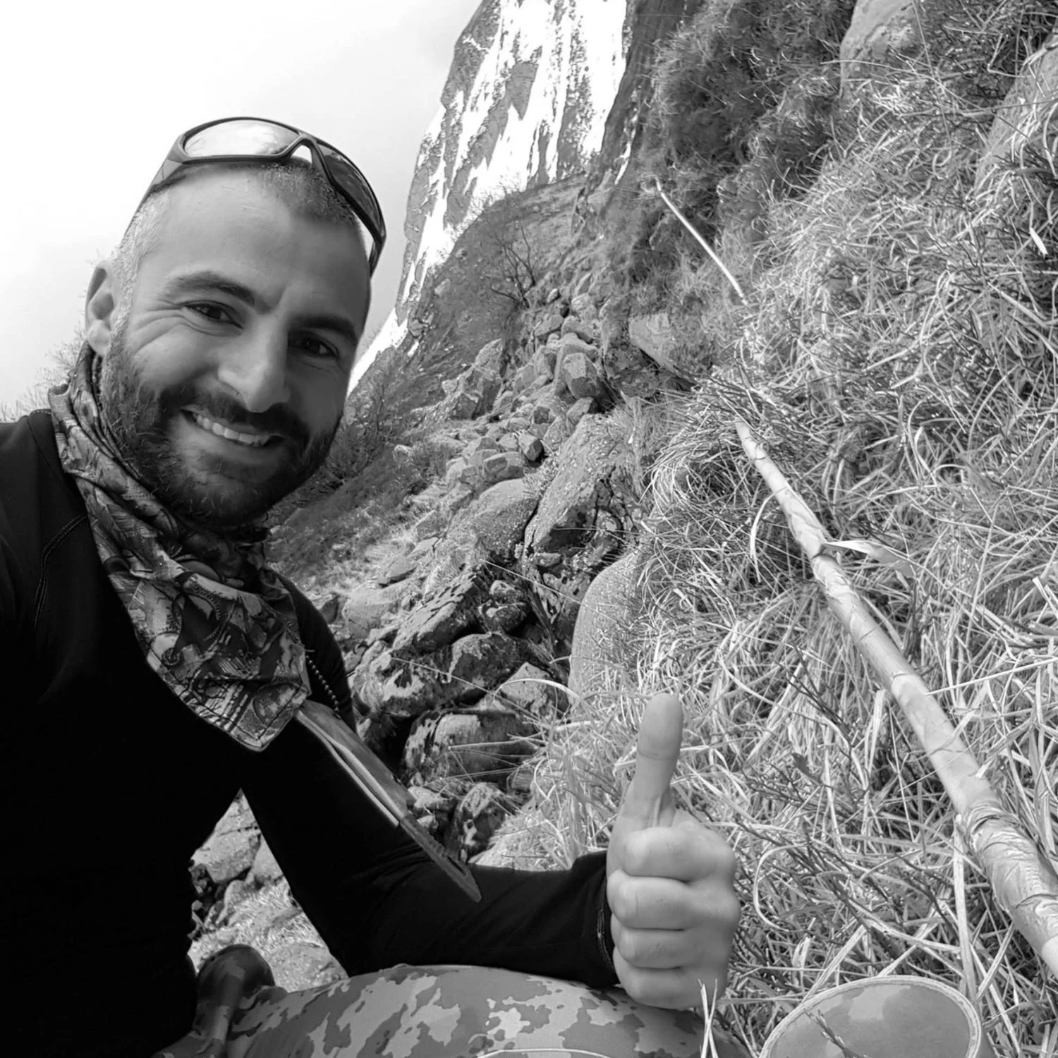 man with sunglasses and scarf giving thumbs up in snow-covered mountainous area
