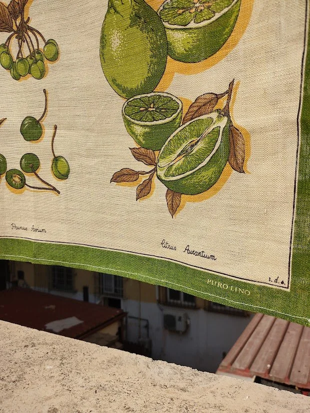 Details on the corner of tea towel with olive green fruit and vegetable printed on gorgeous quality linen