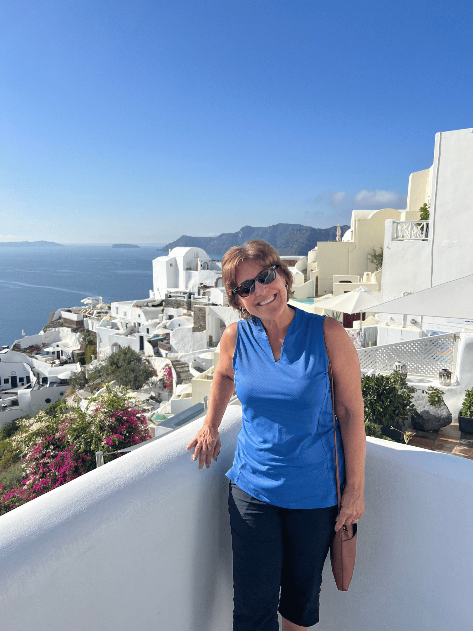 Two women smiling with a view of white buildings and the sea in Santorini, Greece.