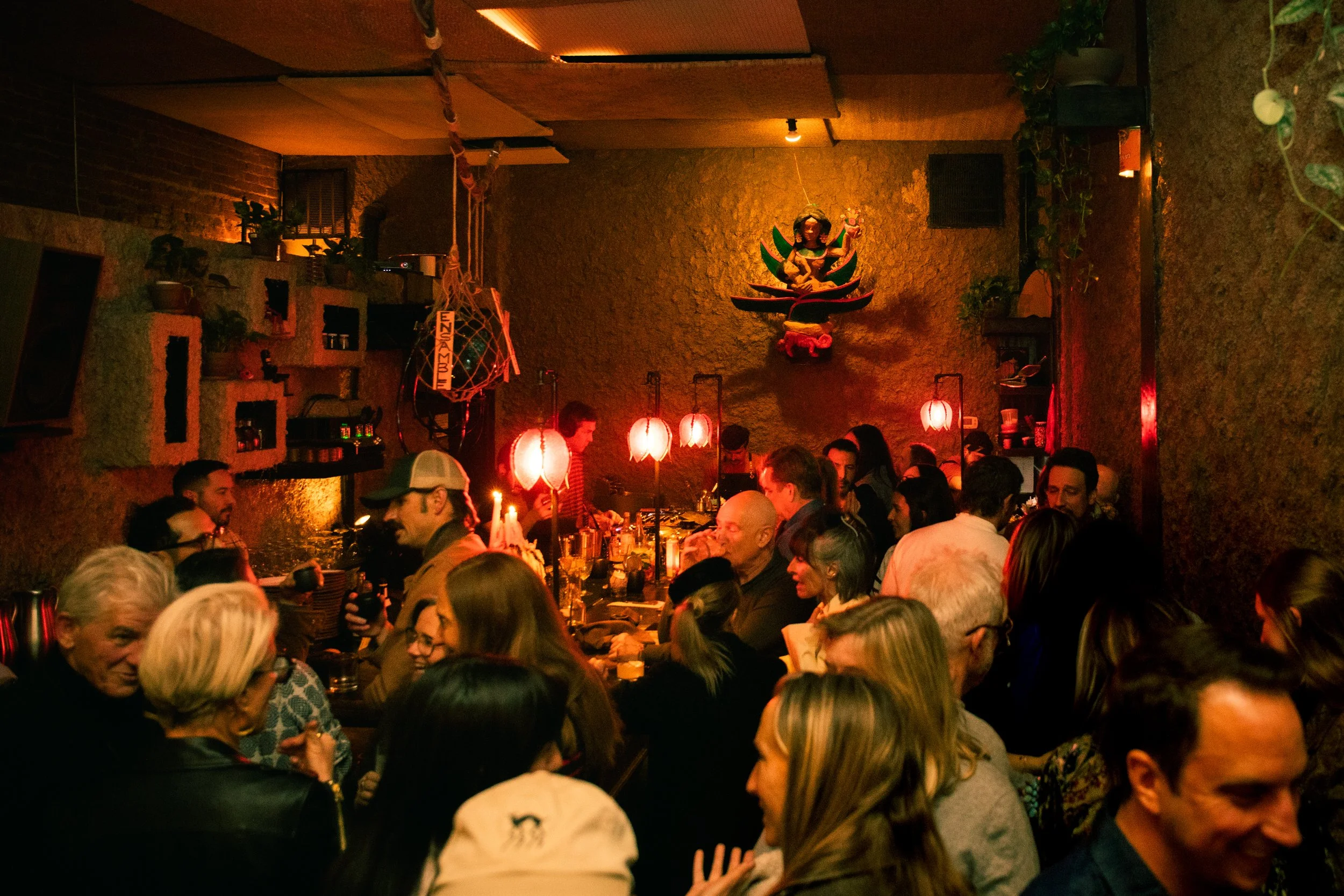 Biennial Culture Club at the Museum of Contemporary Art Denver. People socializing at a celebration with colorful hanging decorations inside a modern room with large windows.