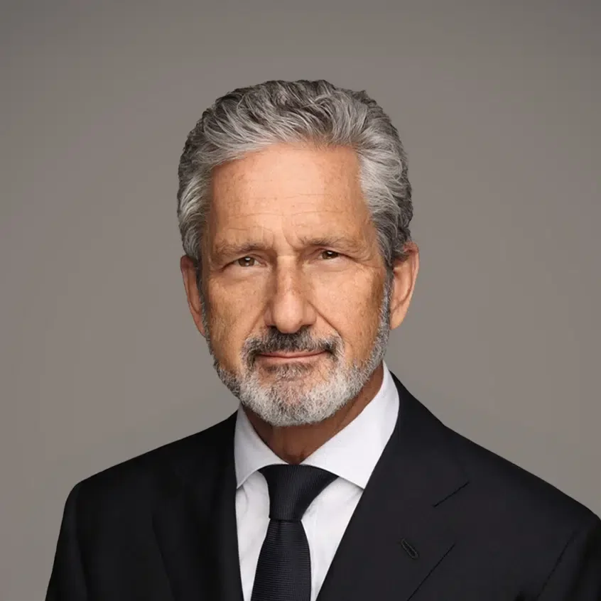 Mike Fries. A smiling man in a dark pinstripe suit, light blue dress shirt, and light blue tie, standing against a blue background.