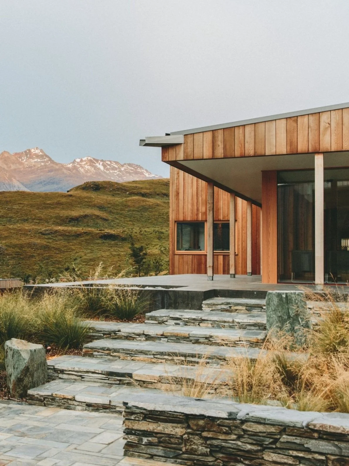 Modern wooden house with stone steps, mountainous landscape, grass