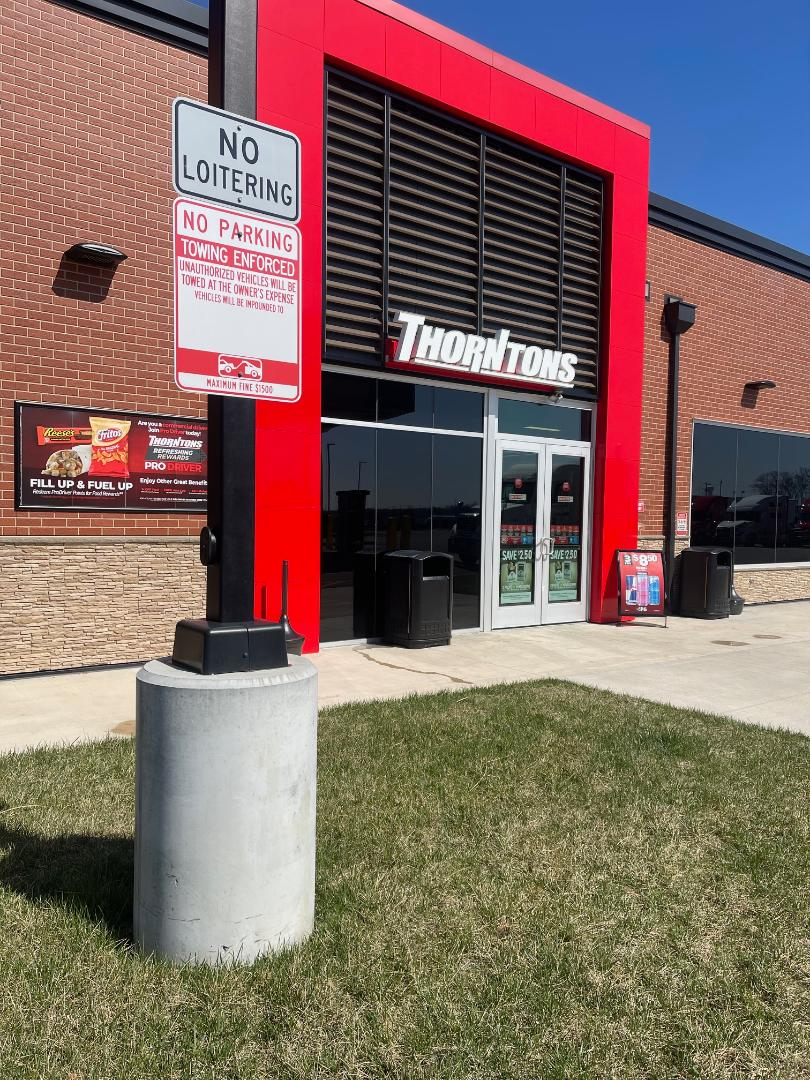 Thornpoons restaurant entrance with glass doors, red framing, and signage. Outside are a No Loitering sign, a No Parking sign, and two trash cans. There is a grass patch in the foreground and clear blue sky.