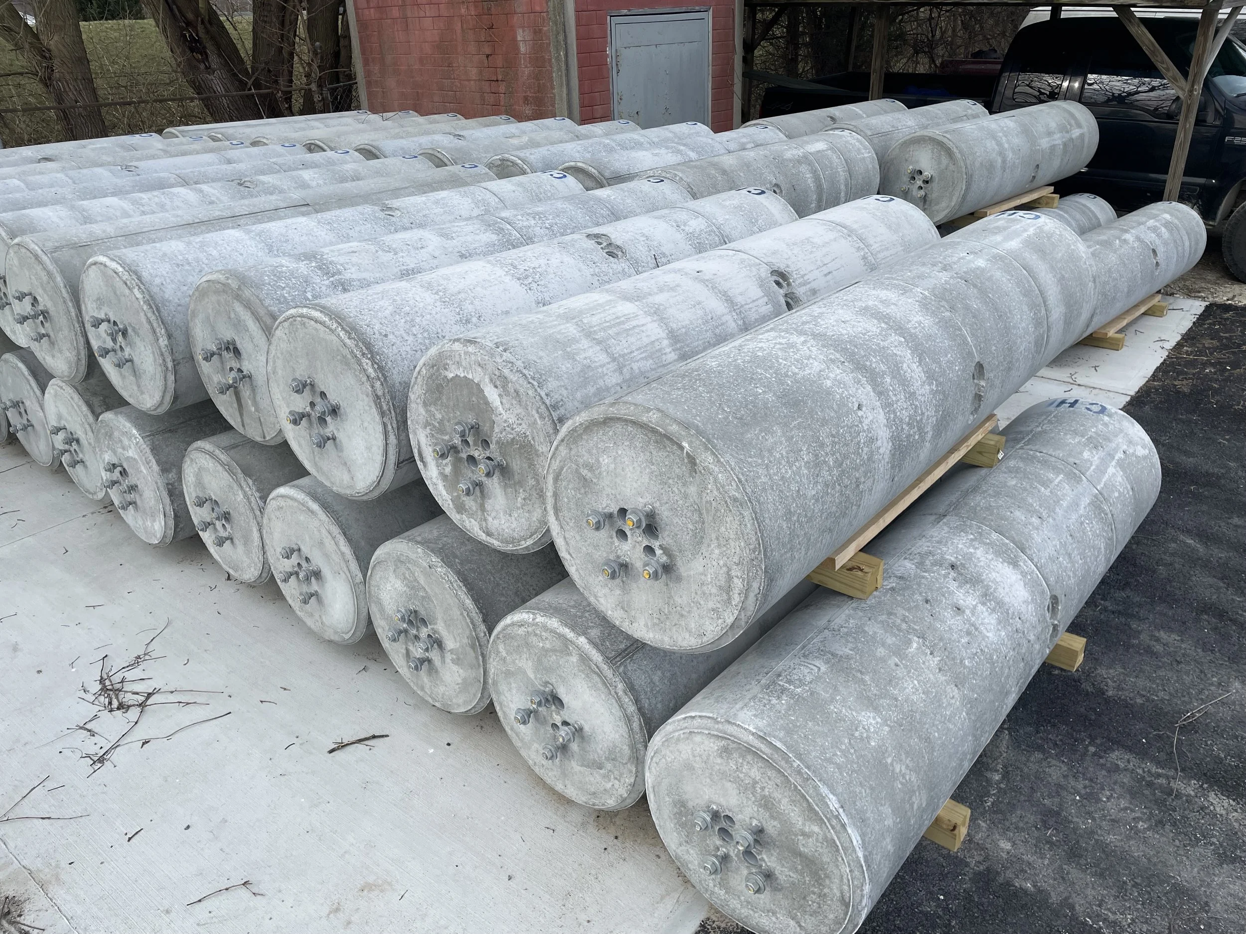 A collection of large, weathered, cylindrical metal tanks stacked on wooden supports outdoors.