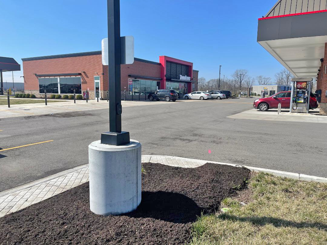 A parking lot outside a modern retail store with a red and gray facade, with cars parked near the entrance, a gas pump, and a clear blue sky.