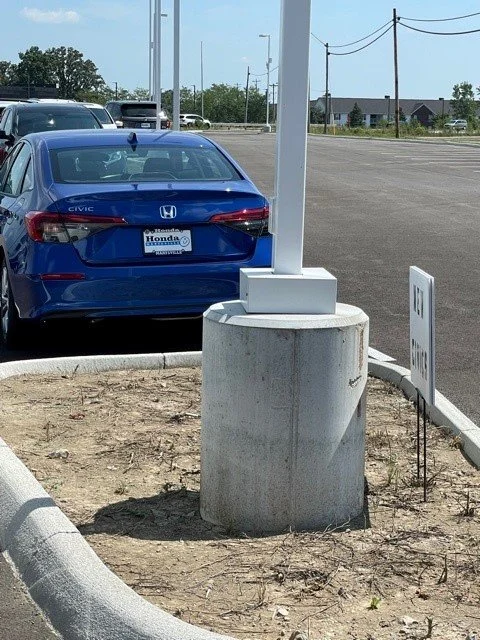 Blue Honda Civic parked in a parking lot near a sidewalk with a white signboard and a pole with a base protector.
