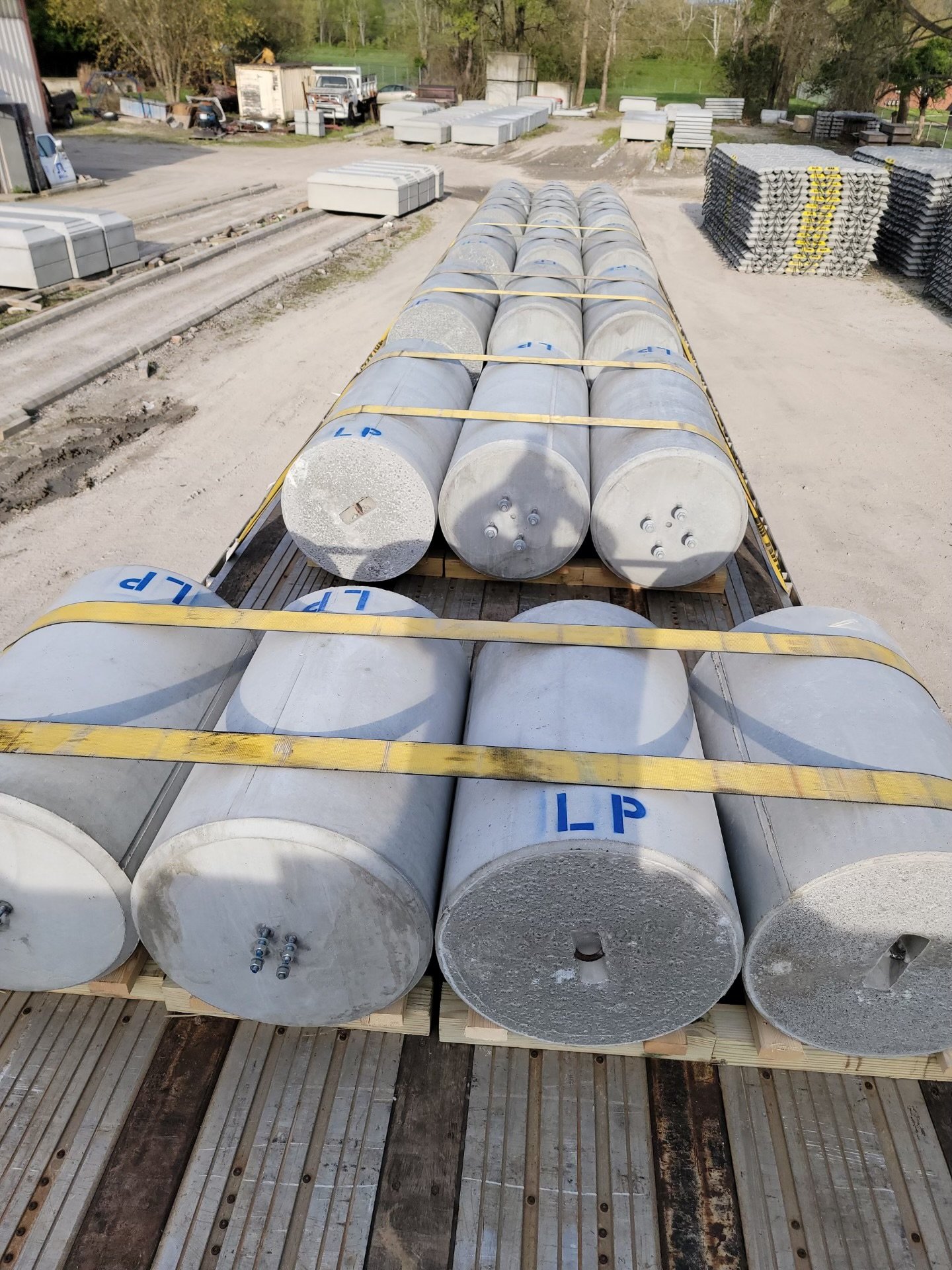 Several large concrete pillars secured with yellow straps on a wooden pallet in an outdoor storage yard.