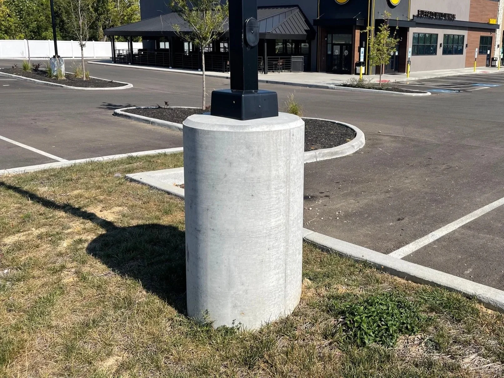 Empty parking lot with a concrete light pole cover and a lamp post, near a restaurant building in the background.