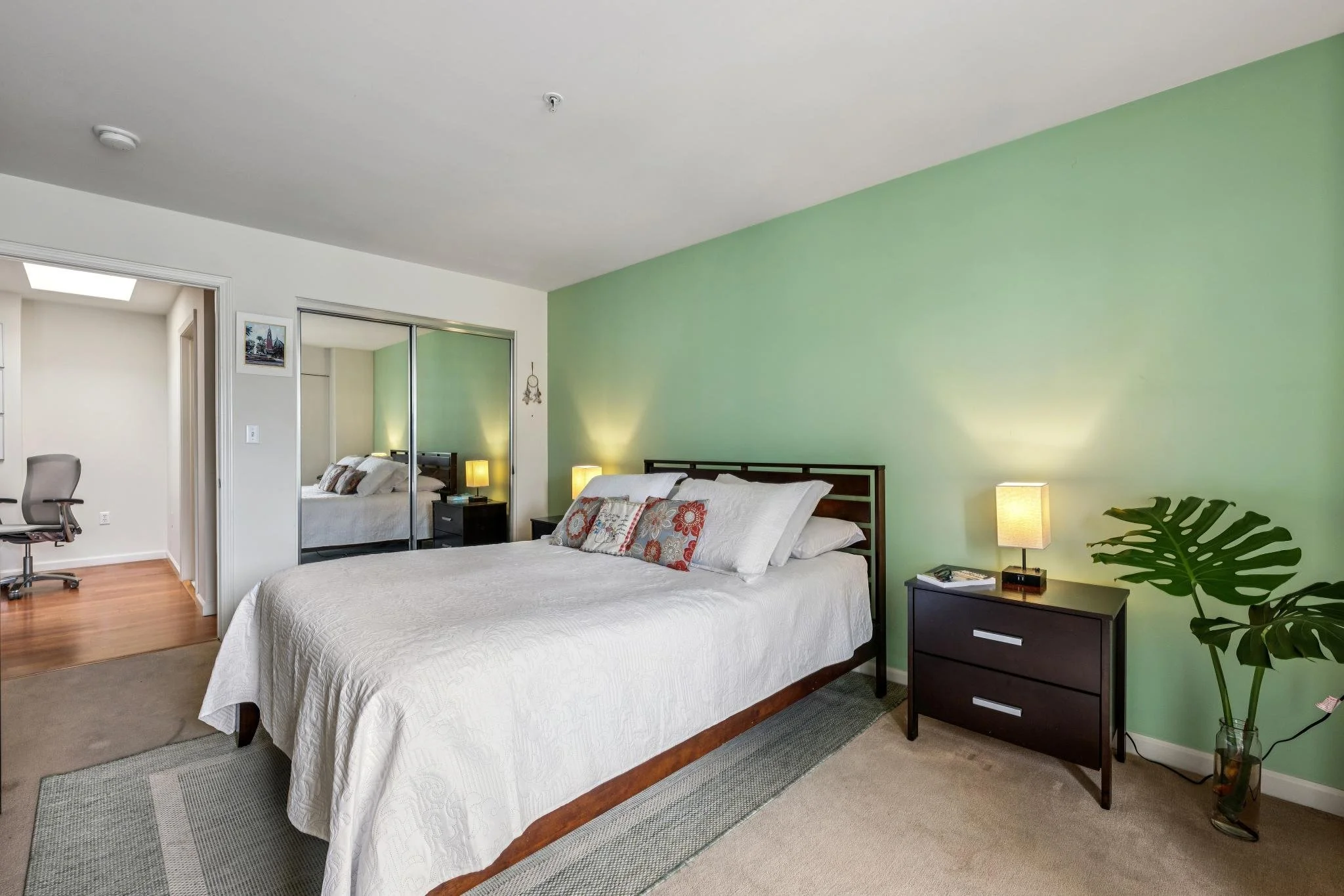  bedroom with a bed, nightstands with lamps, a plant, a mirror, and a window.
