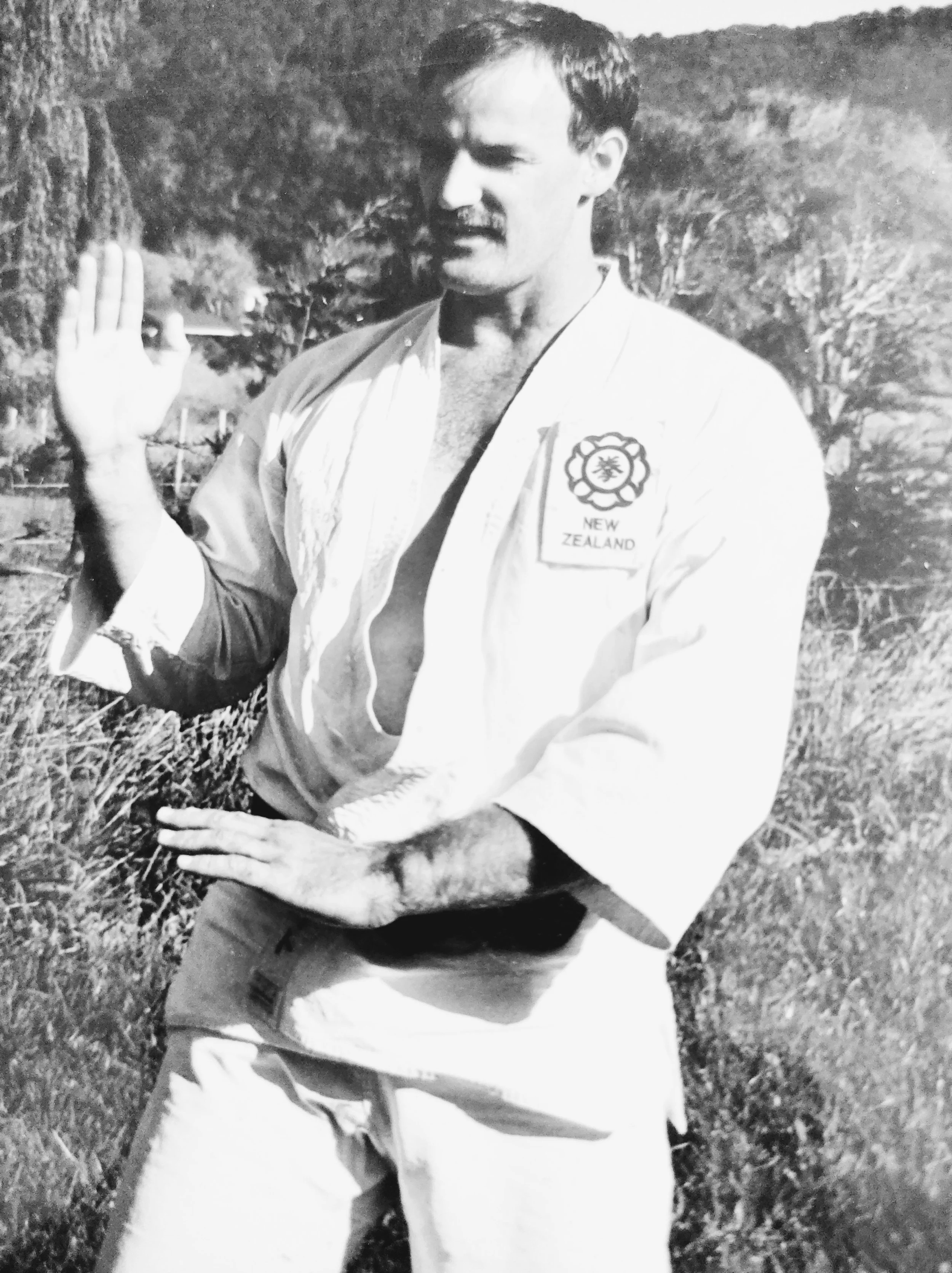A man practicing karate outdoors, wearing a military uniform with a patch that reads 'New Zealand,' making a martial arts pose with one hand raised and the other hand positioned in front.