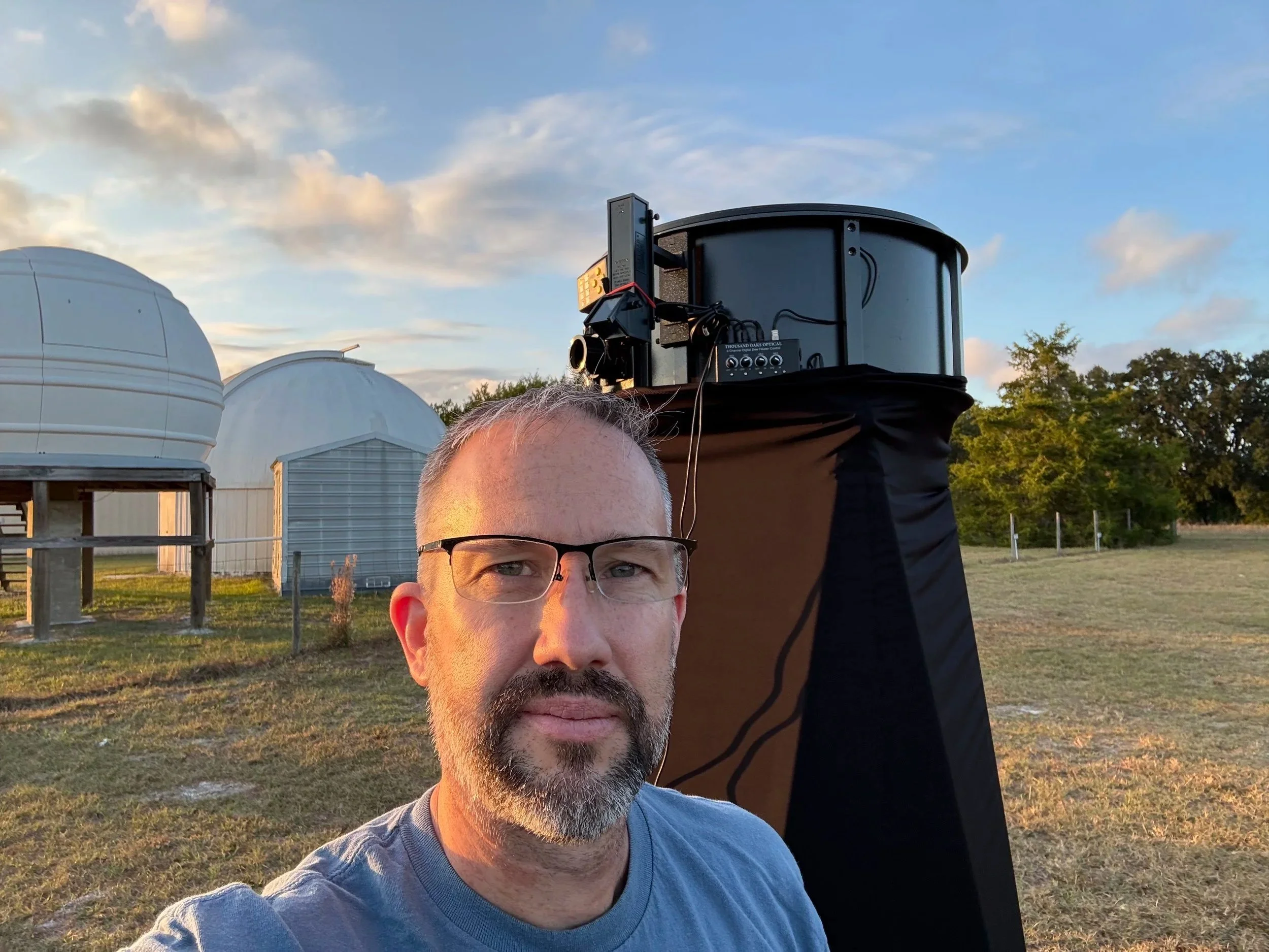Author Joe Barry with large telescope and two observatory domes behind him.
