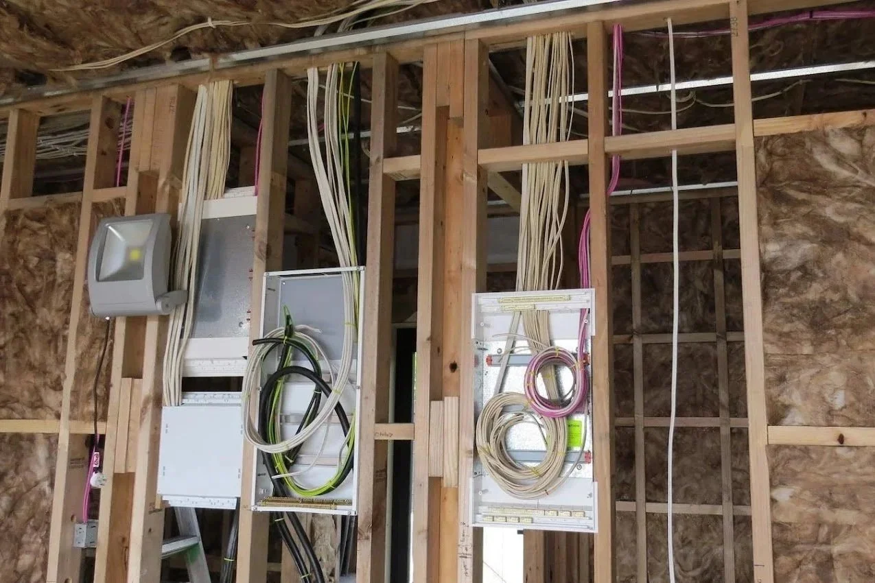 Interior wall framing with electrical wiring and panels installed, with insulation on the wall studs.