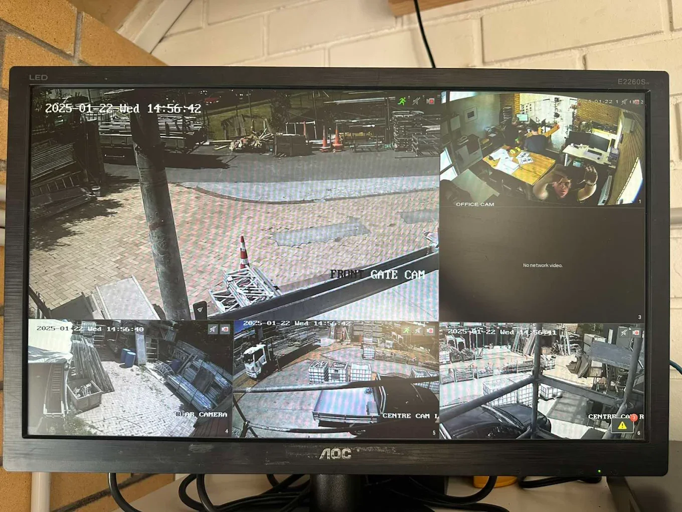 Multiple security camera feeds showing outdoor storage yard and office interior, including a person waving at the camera.