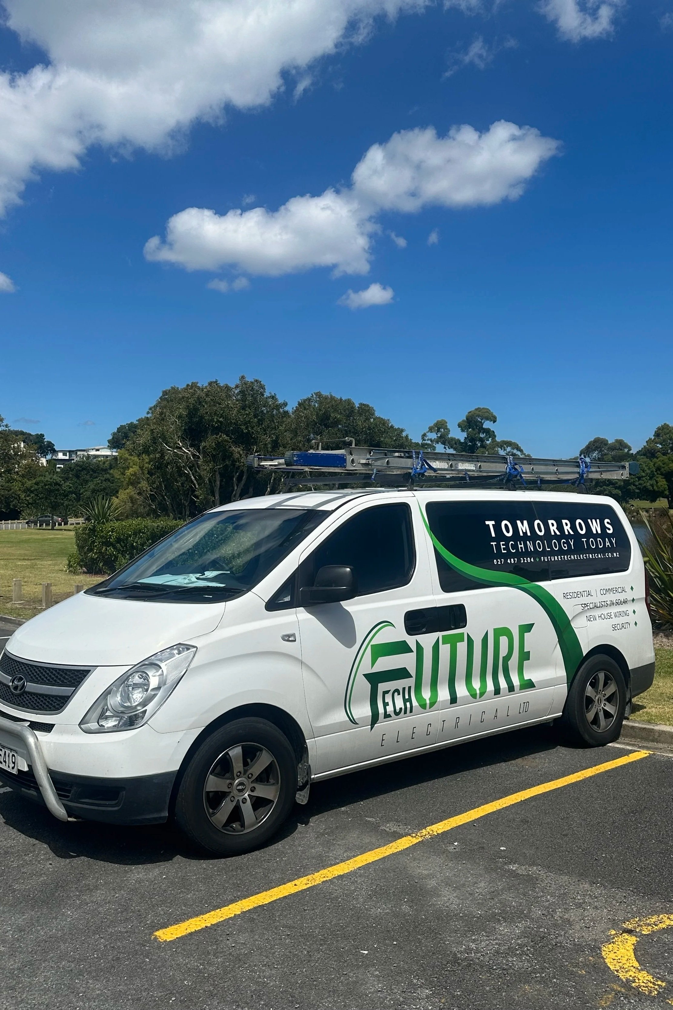 A white van with green and black branding for Future Electrical Ltd. parked on a parking lot, with a ladder on top and a green landscape and blue sky in the background.