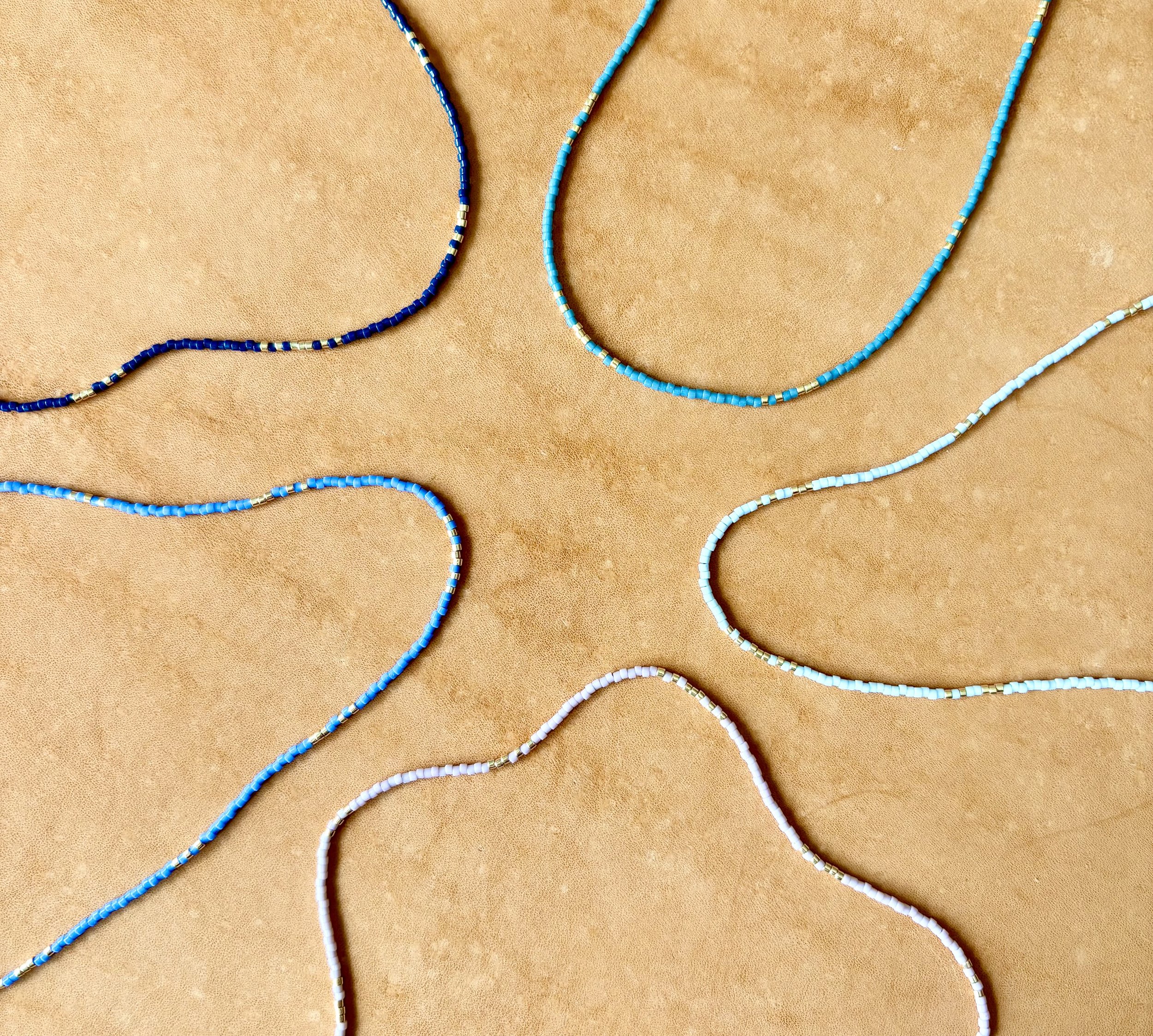 Multiple beaded necklaces in shades of blue and white arranged on a beige surface.
