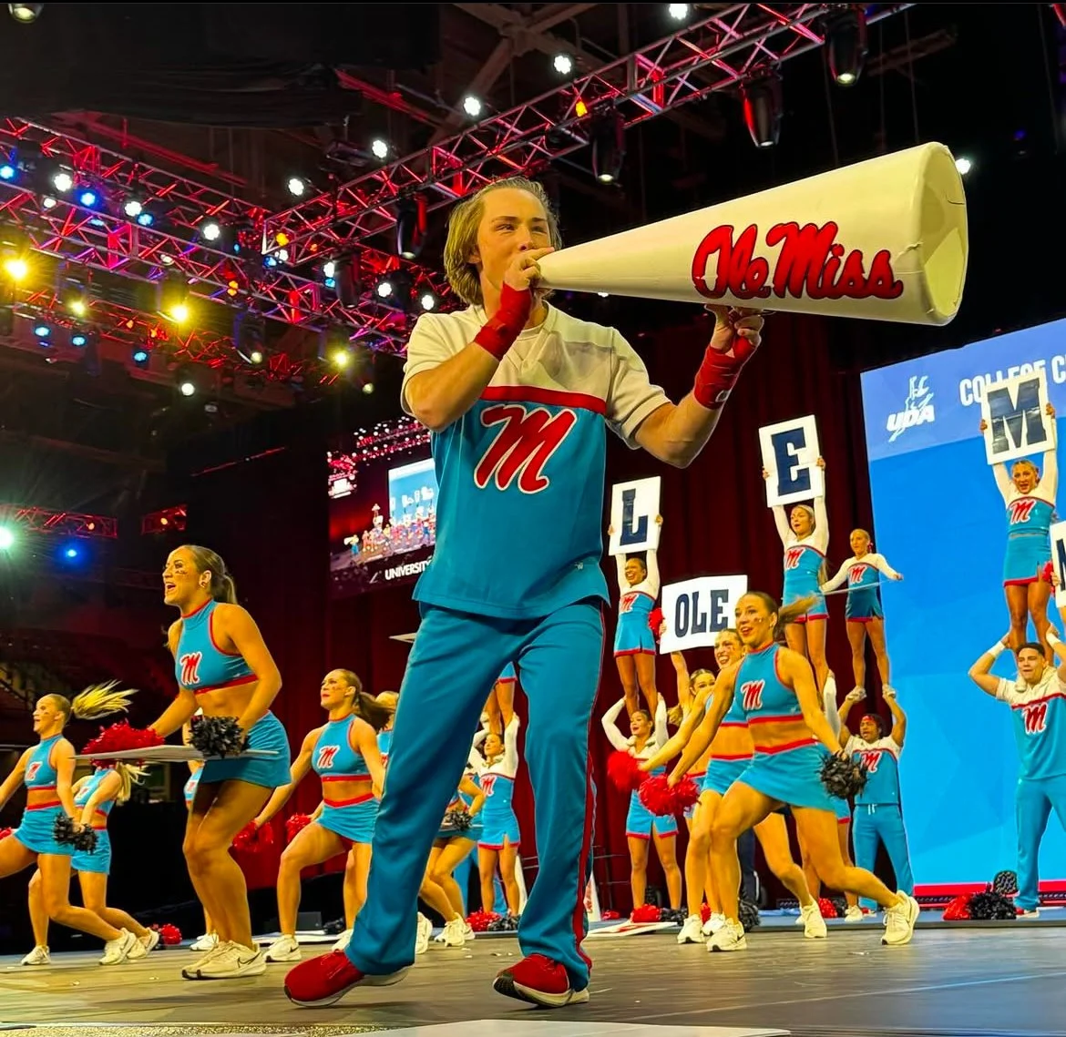 Ole Miss cheerleading team performing with cheerleaders holding signs and a person using a megaphone at a sports event.