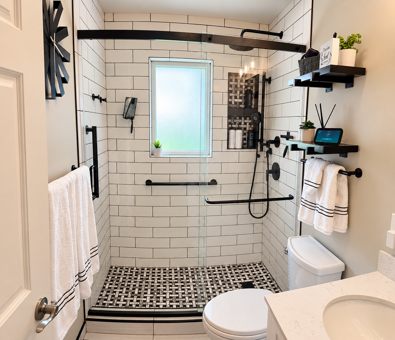 Modern bathroom with white subway tile, glass-enclosed walk-in shower, black fixtures, patterned floor tile, toilet, and vanity.
